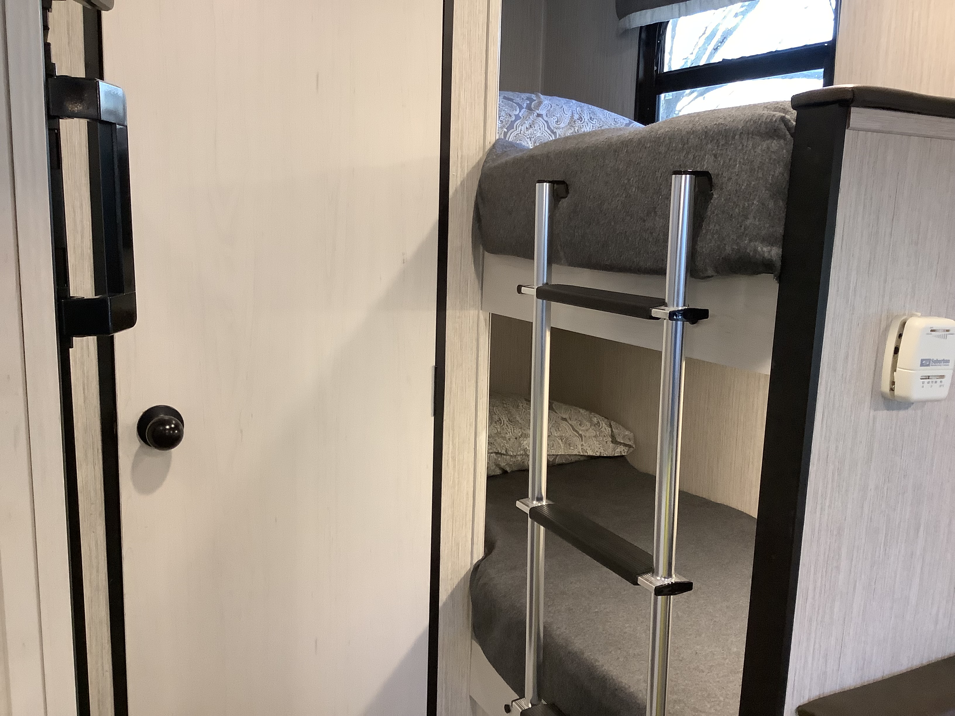 Inside an RV rental, showing a cozy bunk bed sleeping area with a ladder, a door, and a wall-mounted thermostat.. Other Other 2021