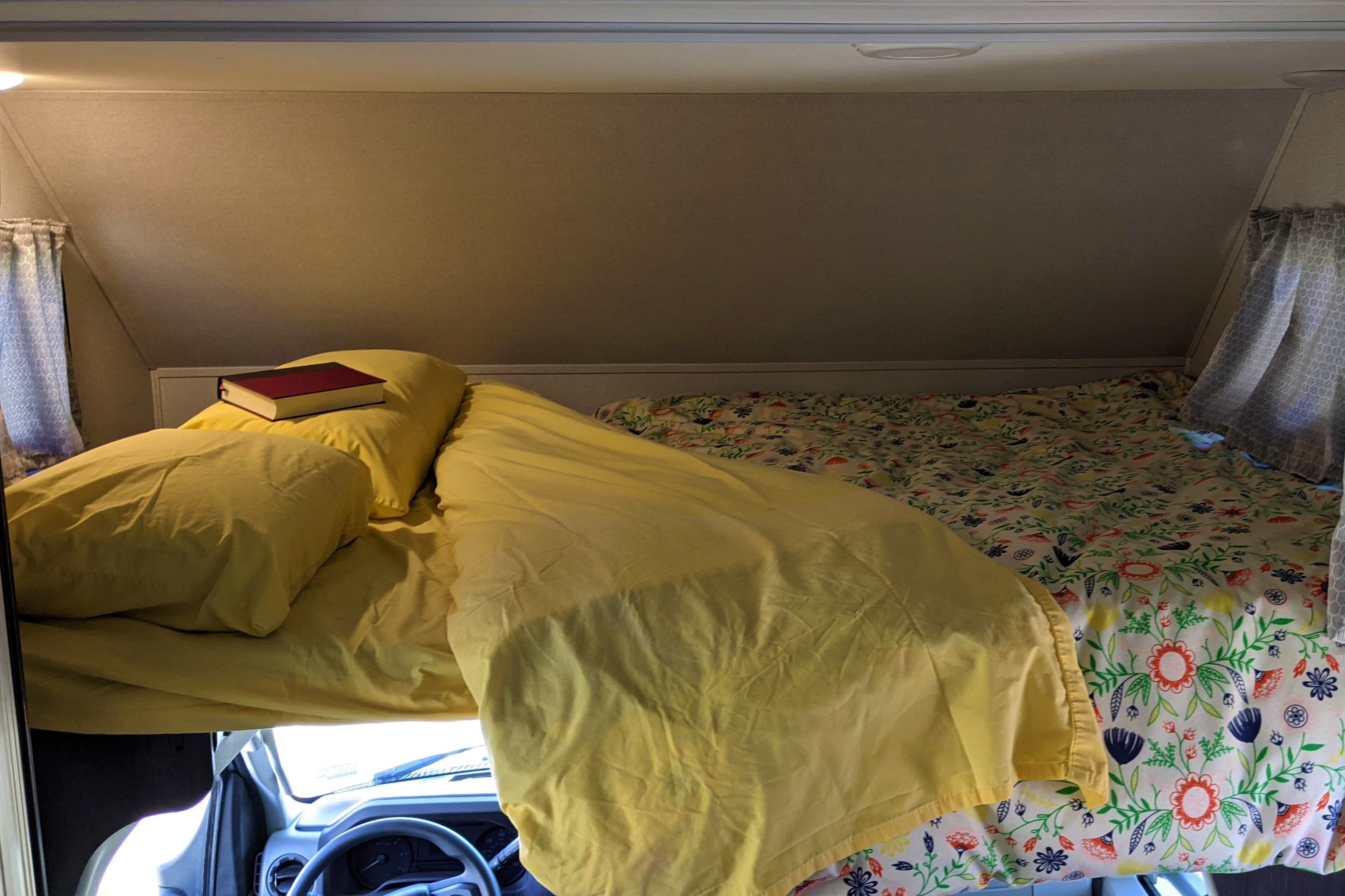Over-cab bunk in an RV rental, featuring yellow and floral bedding, perfect for a cozy night's sleep.. Forest River Sunseeker LE 2021