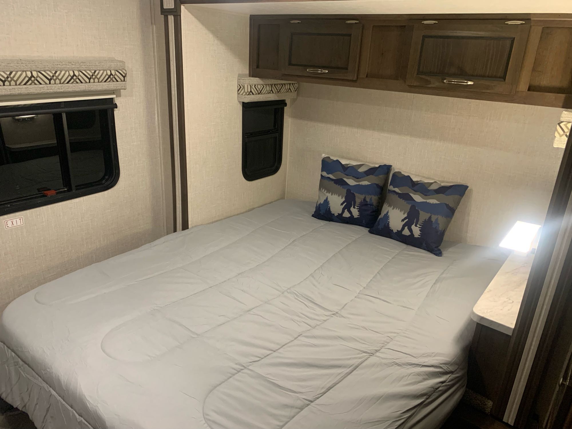RV rental bedroom interior features a bed, Bigfoot pillows, overhead cabinets, and window.. Forest River Coachmen Prism 2020