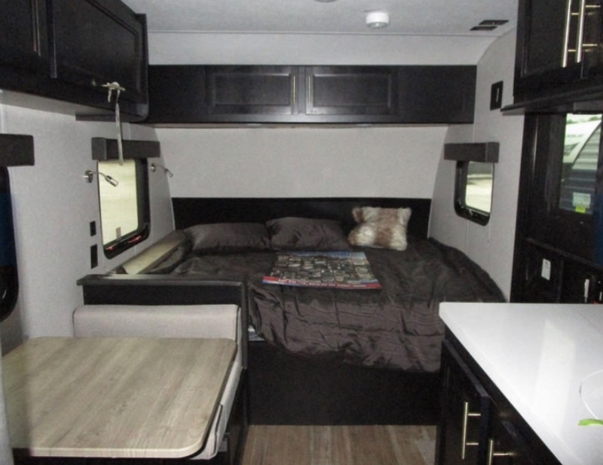 Modern RV rental interior: bedroom with overhead cabinets, side windows, and a compact dining area.. Forest River Cherokee Wolf Pup Black Label 2022
