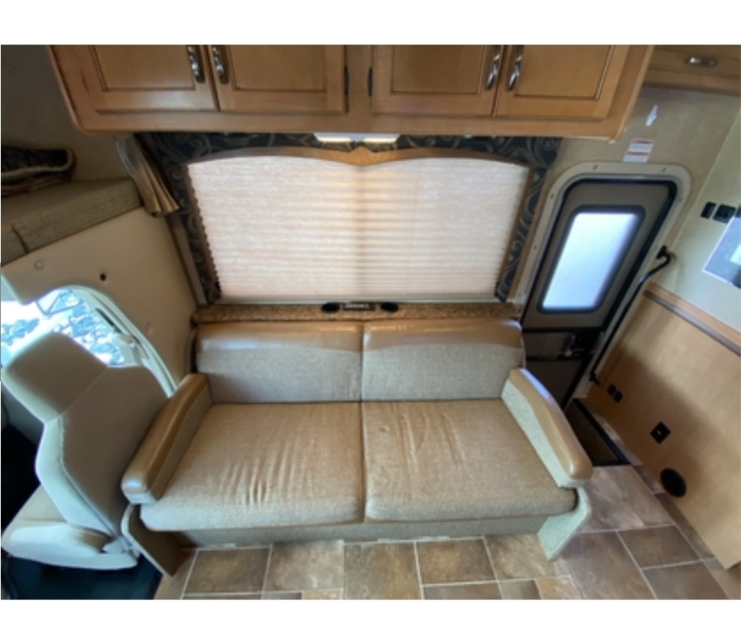 Spacious RV rental interior features a two-seater sofa, large window, and overhead storage, perfect for travel.. Thor Four Winds 2016