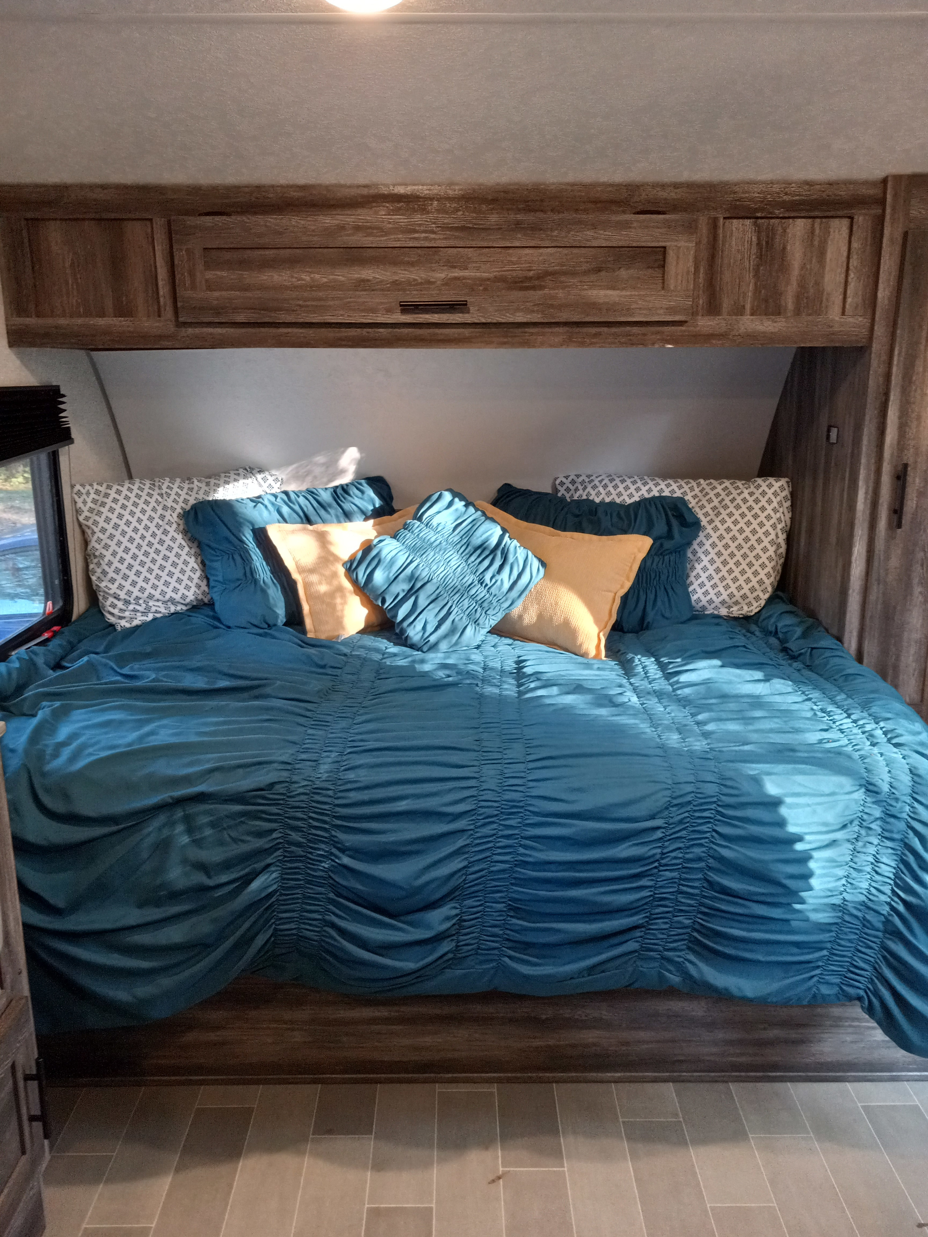 Cozy RV rental bedroom with a blue comforter, accent pillows, and wood cabinets.. Forest River Salem FSX PLATINUM 2020