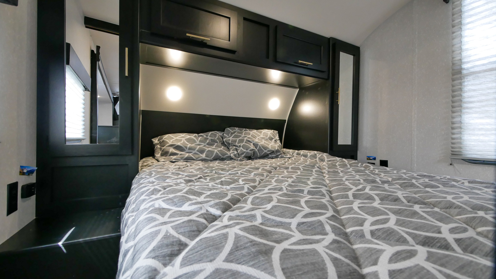 RV rental bedroom: a cozy bed with patterned linens, dark overhead cabinets, integrated lights, and mirrored wardrobes.. Forest River Cherokee Grey Wolf 2022