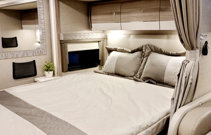 Spacious RV rental bedroom with a neutral-toned bed, storage, window, and mirror. Perfect for road trip comfort.. Thor Delano 2021