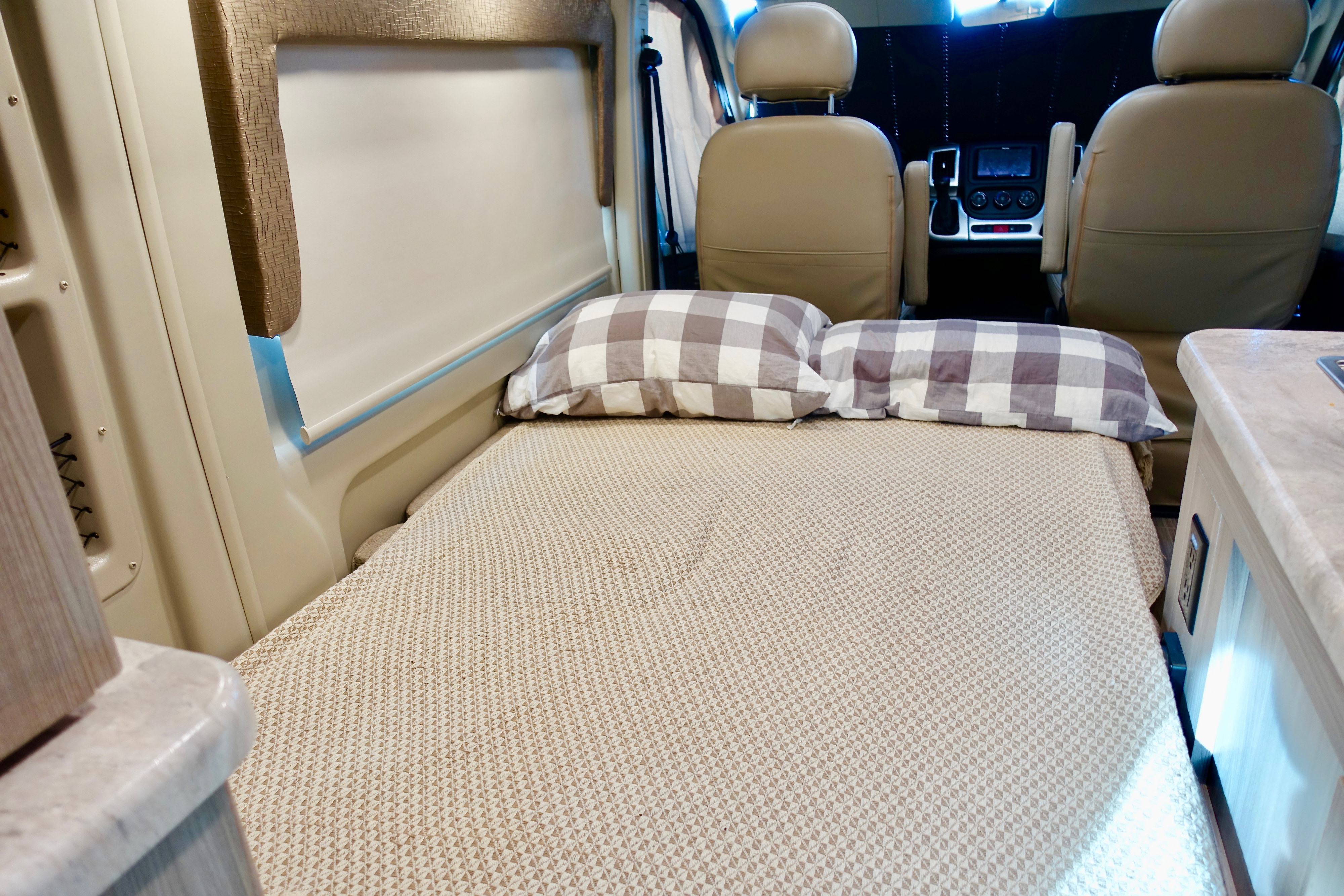 Comfortable RV rental interior with a made bed, plaid pillows, and front cabin seats visible.. Thor Motor Coach Scope 18M 2022