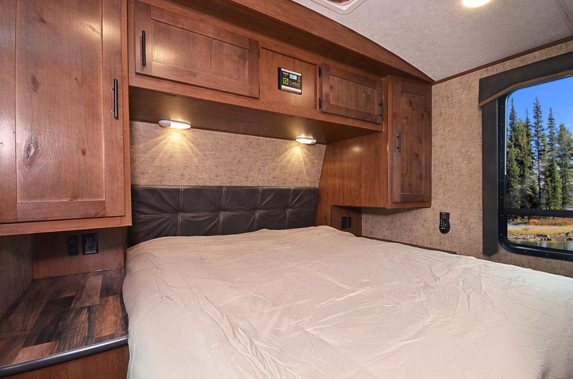 RV rental bedroom: Comfortable bed, wood cabinets, control panel, and a scenic window view for your travels.. Outdoors RV 23DBS 2022