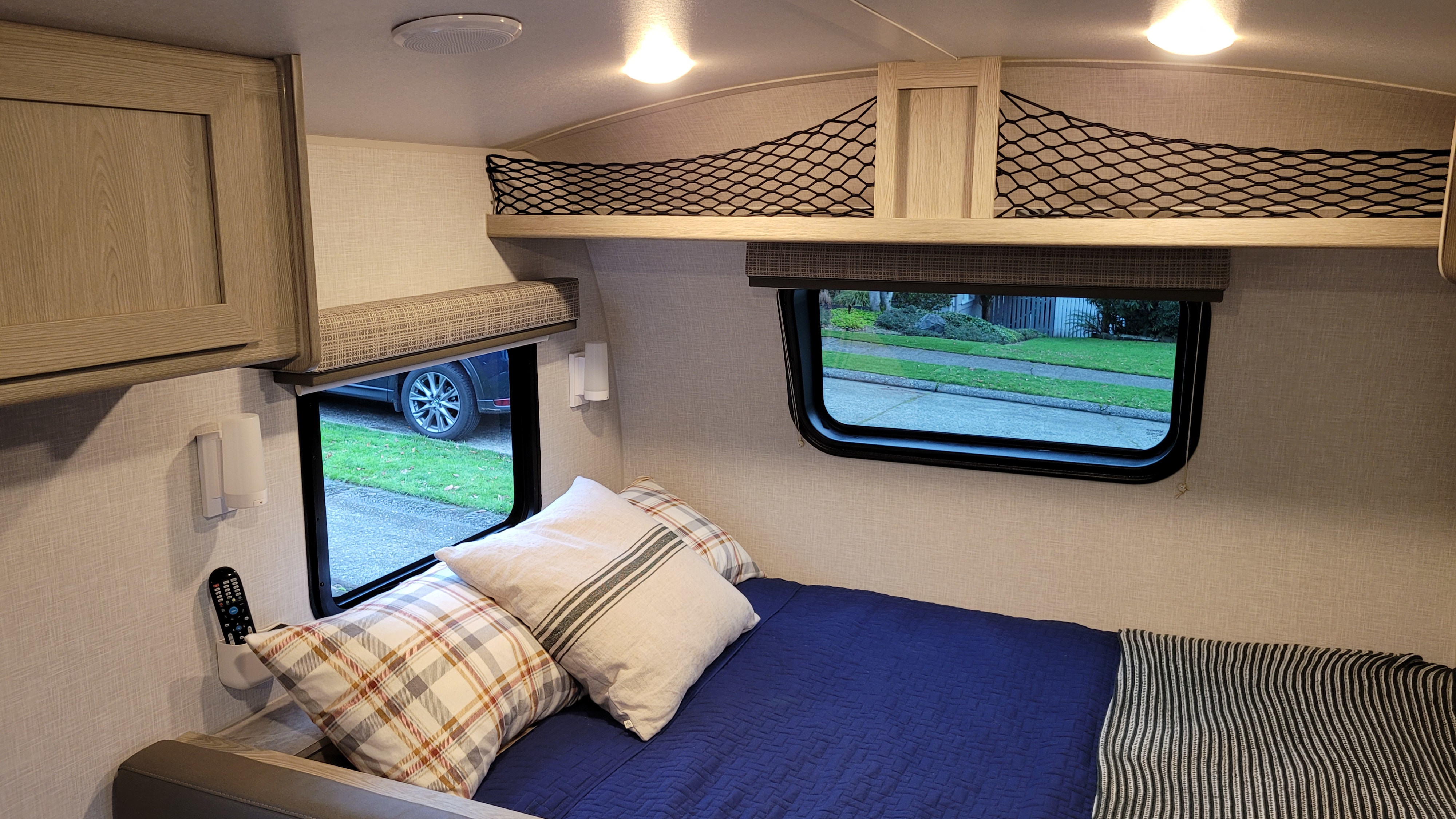 Cozy RV rental bedroom with blue bed, plaid pillows, windows to outside, & overhead storage. Ready for adventure!. Forest River Flagstaff E-Pro 2021