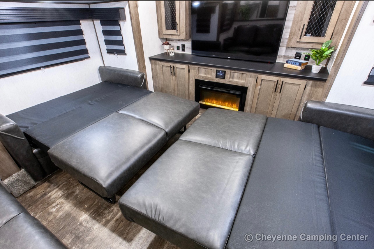 Spacious RV rental interior featuring convertible sofas that extend into comfortable beds, alongside a cozy fireplace and TV setup.. Forest River Sabre 2021