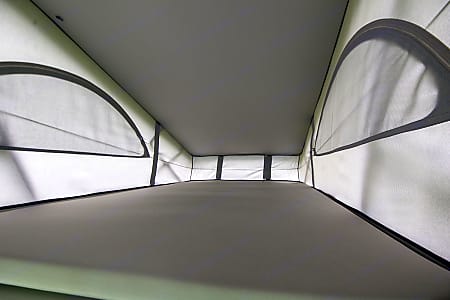 Cozy pop-up roof sleeping area inside an RV rental. Features mesh windows & flat bed for camping comfort.. VW California Ocean 2024
