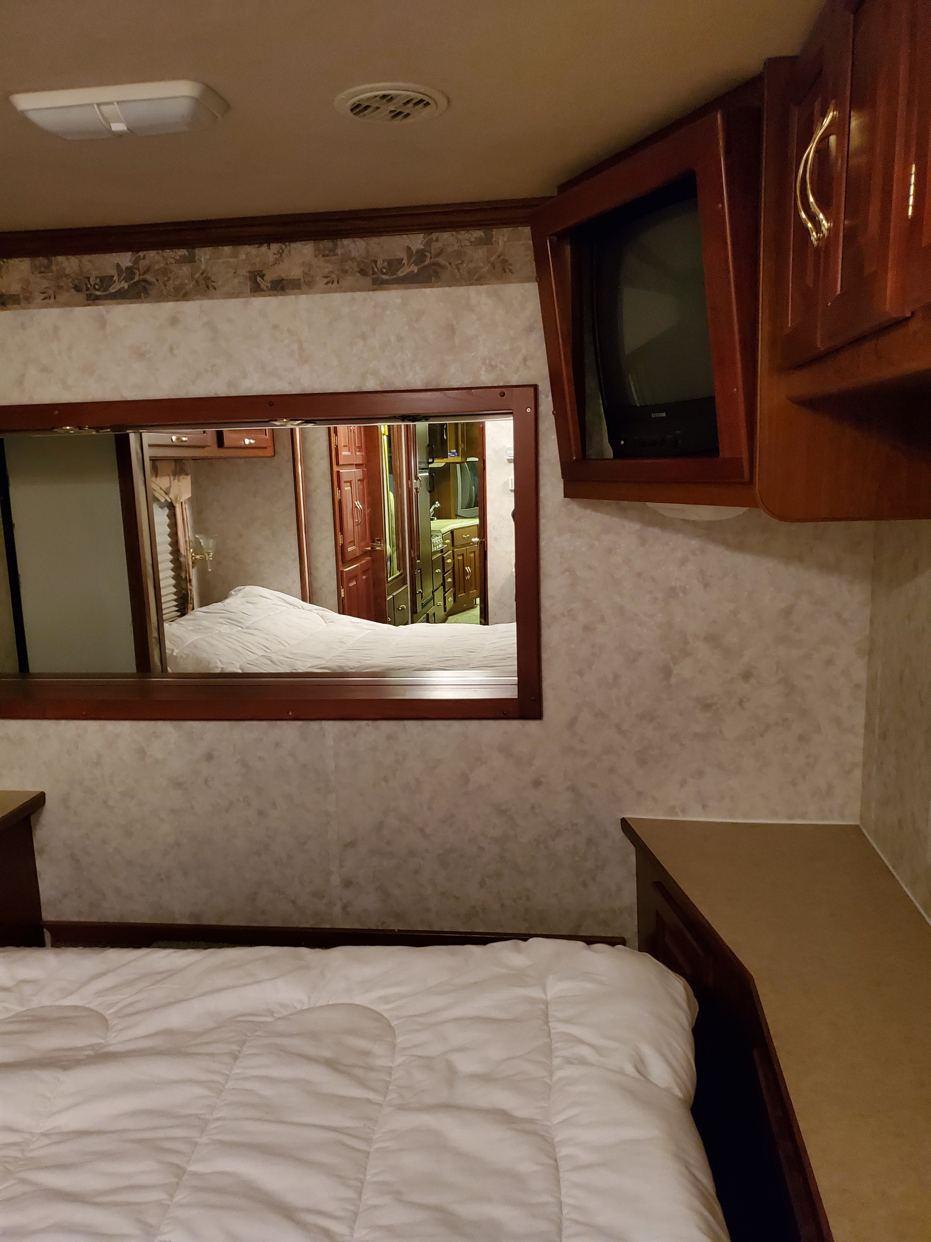Comfortable RV rental bedroom with a white comforter, mirror reflecting the living area, and wall-mounted TV.. Coachmen Cross Country Elite 2003
