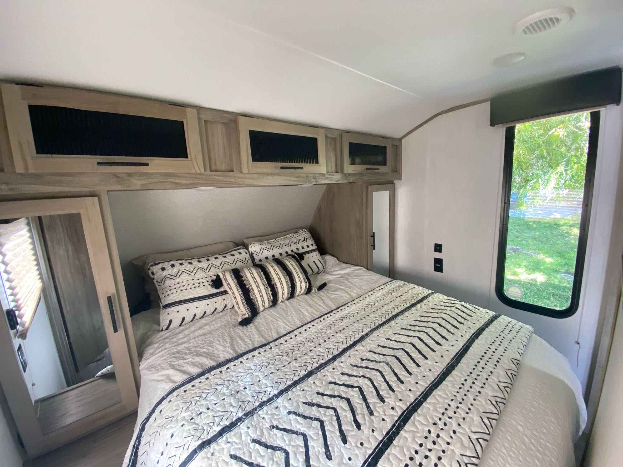 Cozy RV rental bedroom with modern decor, comfy bed, overhead cabinets, & scenic window view. Perfect for adventure!. Forest River Cherokee Alpha Wolf 2021