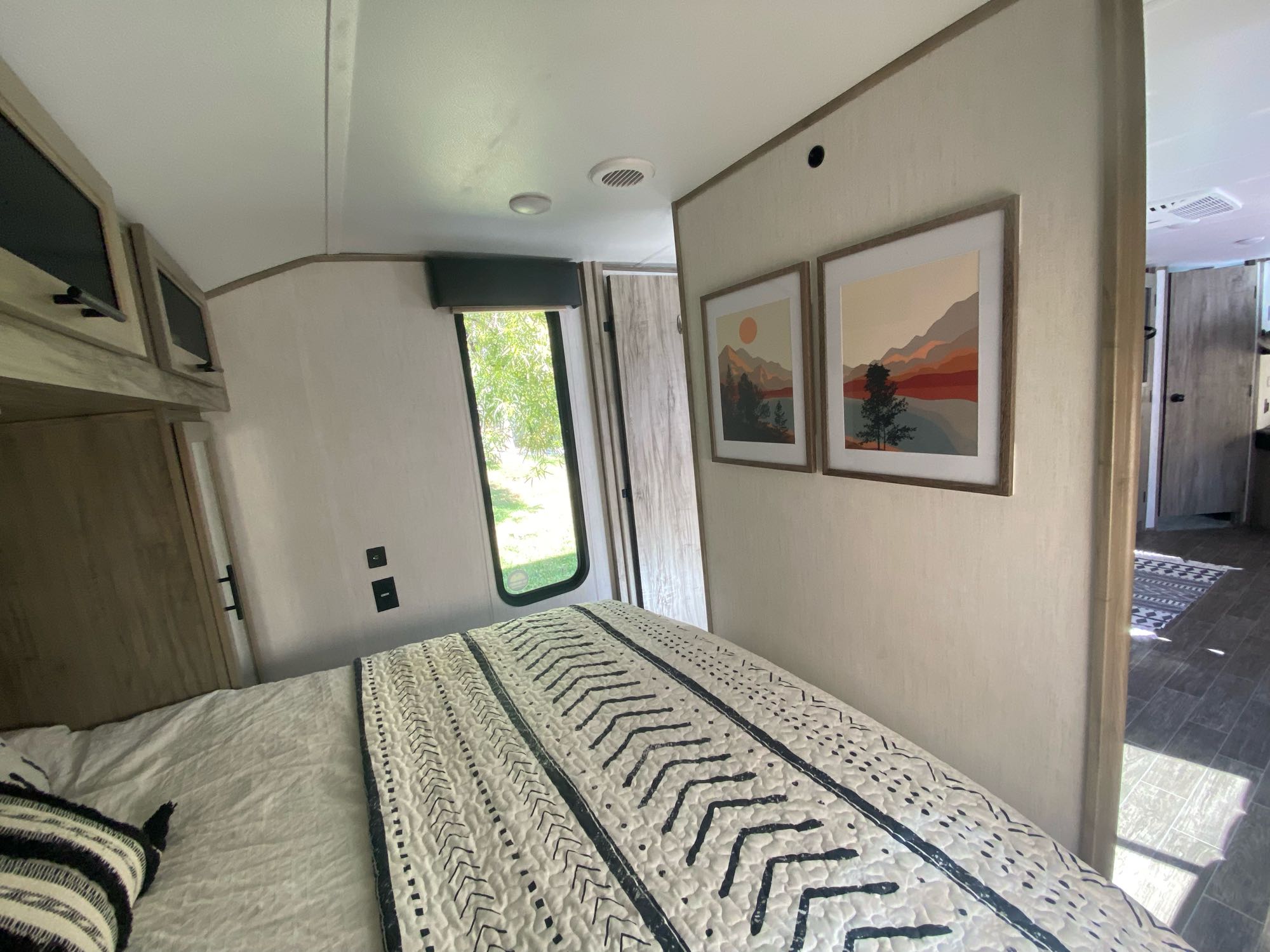 Cozy RV rental bedroom with patterned bed, mountain art, and bright window. Perfect for your next adventure.. Forest River Cherokee Alpha Wolf 2021