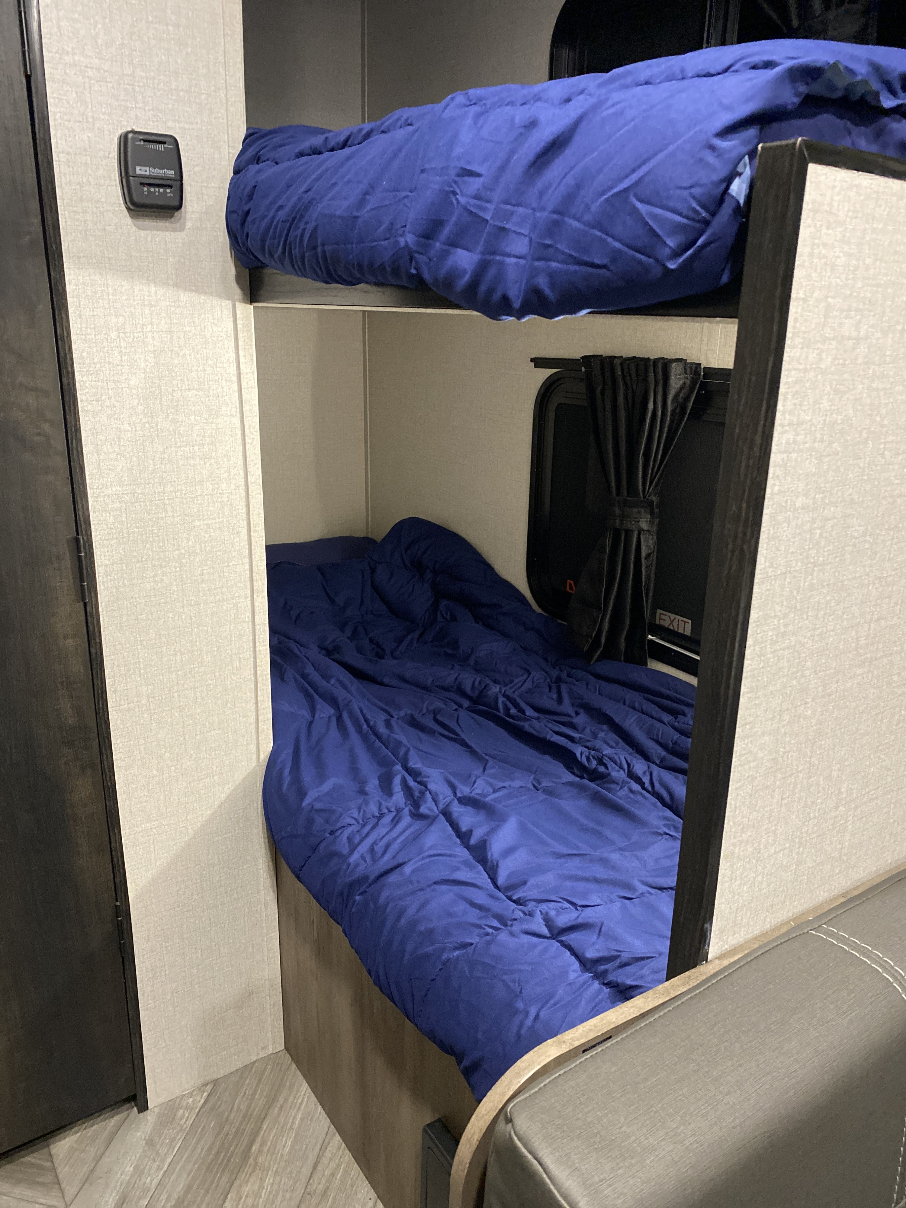 RV rental bunk beds with blue bedding, a wall-mounted thermostat, and an emergency exit window with black curtains for trips.. Highland ridge 19bh 2022