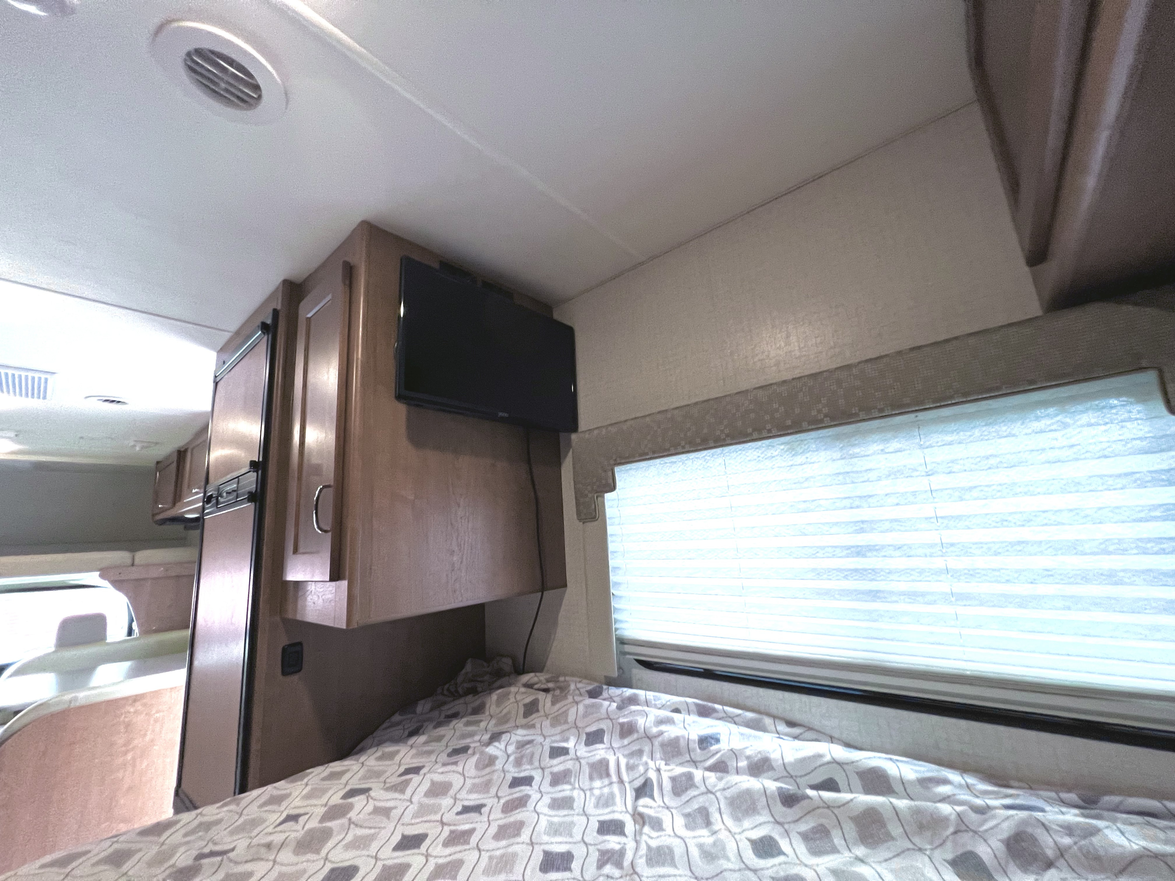 Cozy RV rental sleeping nook: A bed with patterned comforter, mounted TV, and window with blinds.. Winnebago Minnie Winnie 2020