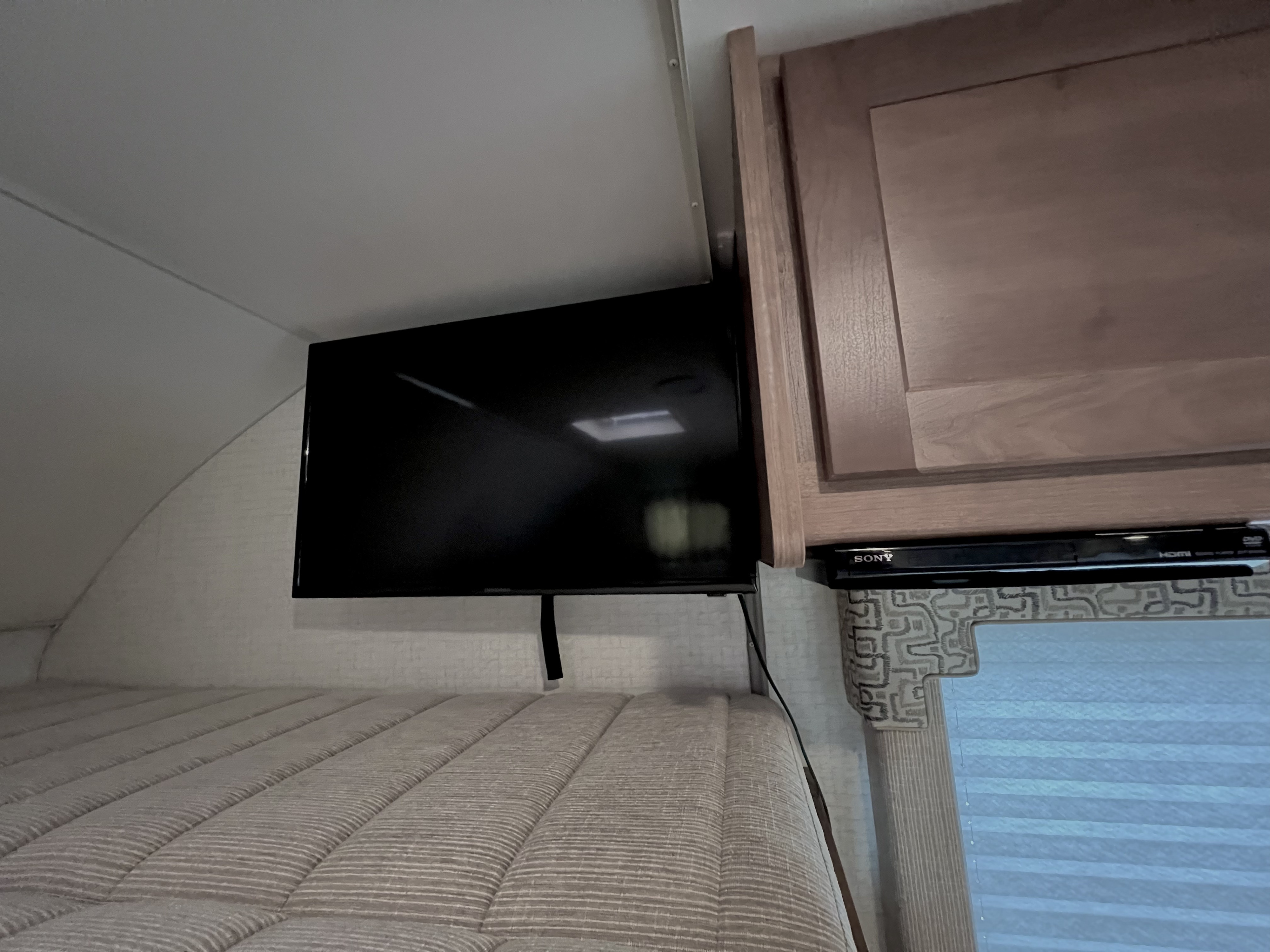 Enjoy an RV rental! This cozy sleeping area features a bed, wall-mounted TV, and DVD player for entertainment.. Winnebago Minnie Winnie 2020