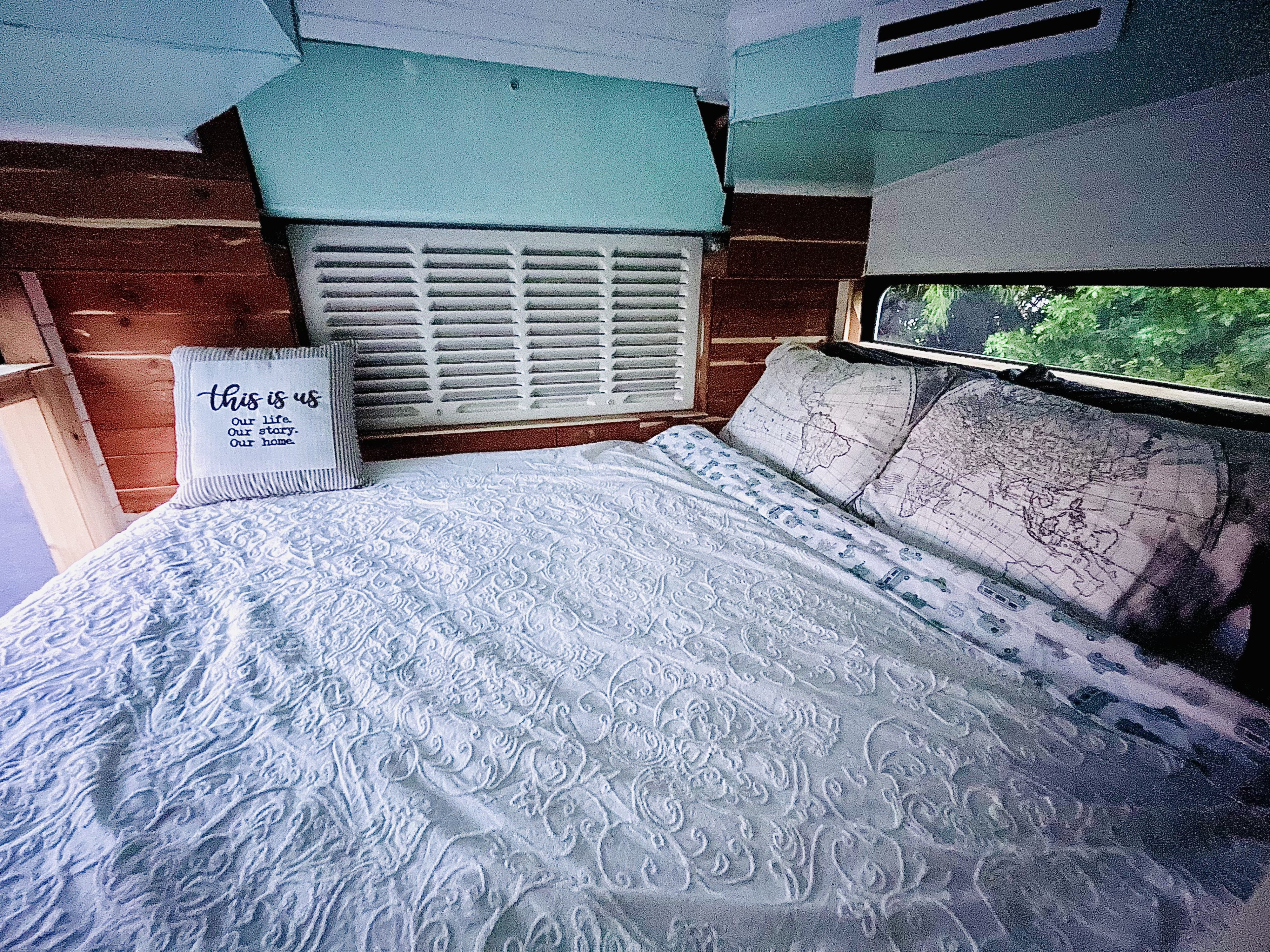 Cozy RV rental bedroom featuring a comfy bed, patterned blue comforter, and map-themed pillows.. Gillig Low Floor 2021