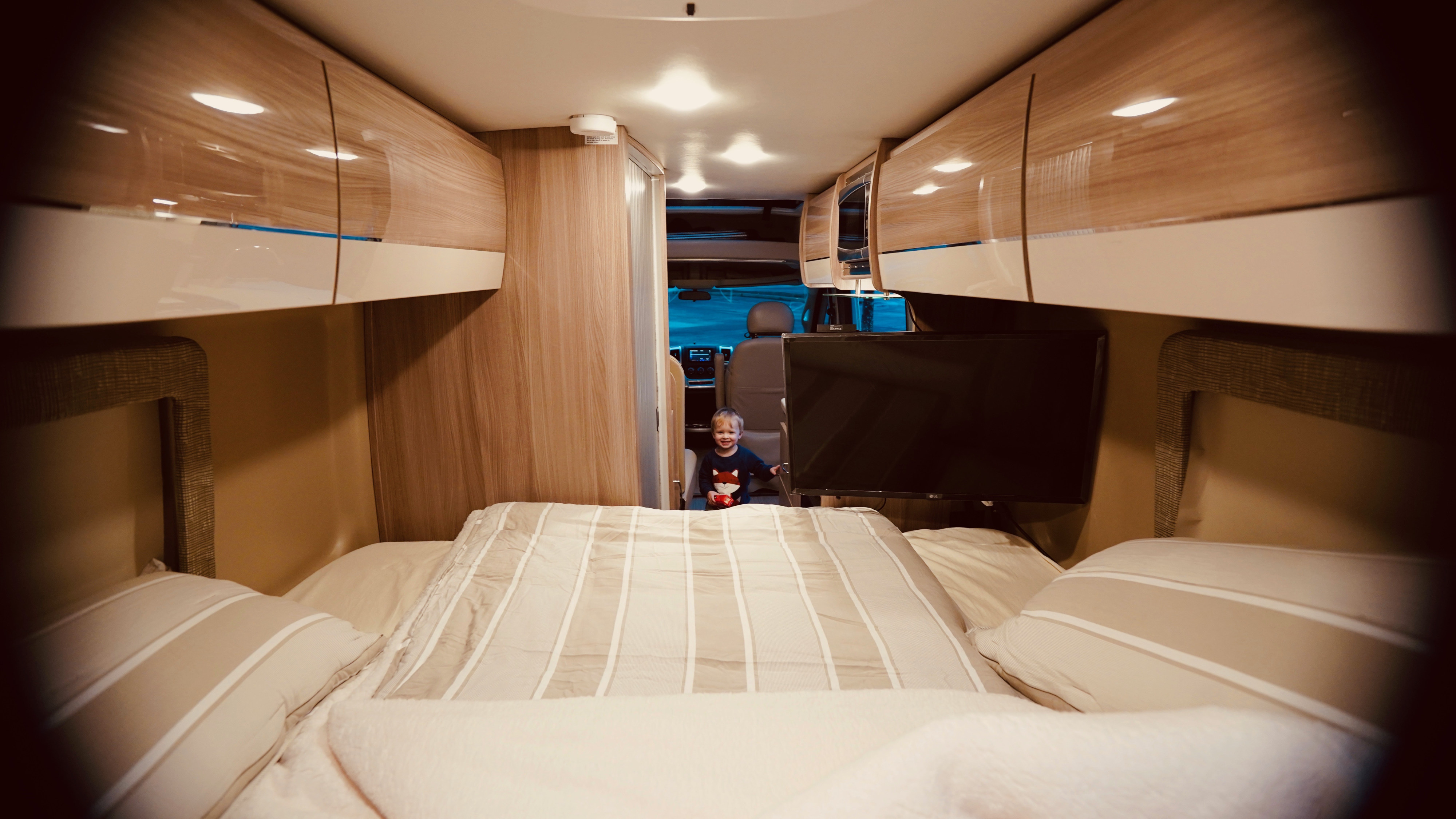 Cozy RV rental interior: A happy child stands near the front, framed by a bed, sleek cabinets, and a mounted TV. Ideal for family road trips.. Thor Motor Coach Sequence 20A 2022