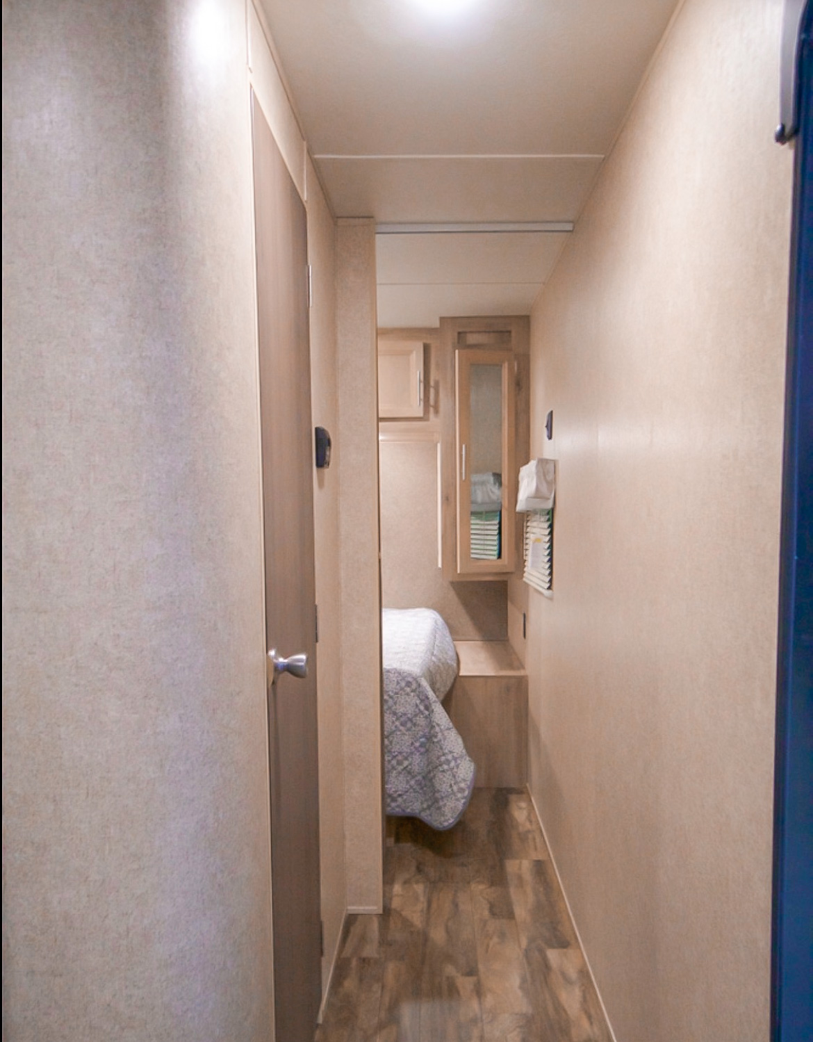 Inside an RV rental, a narrow hallway leads to a bedroom area with a bed, wood cabinetry, and laminate flooring.. Coachmen Other 2019