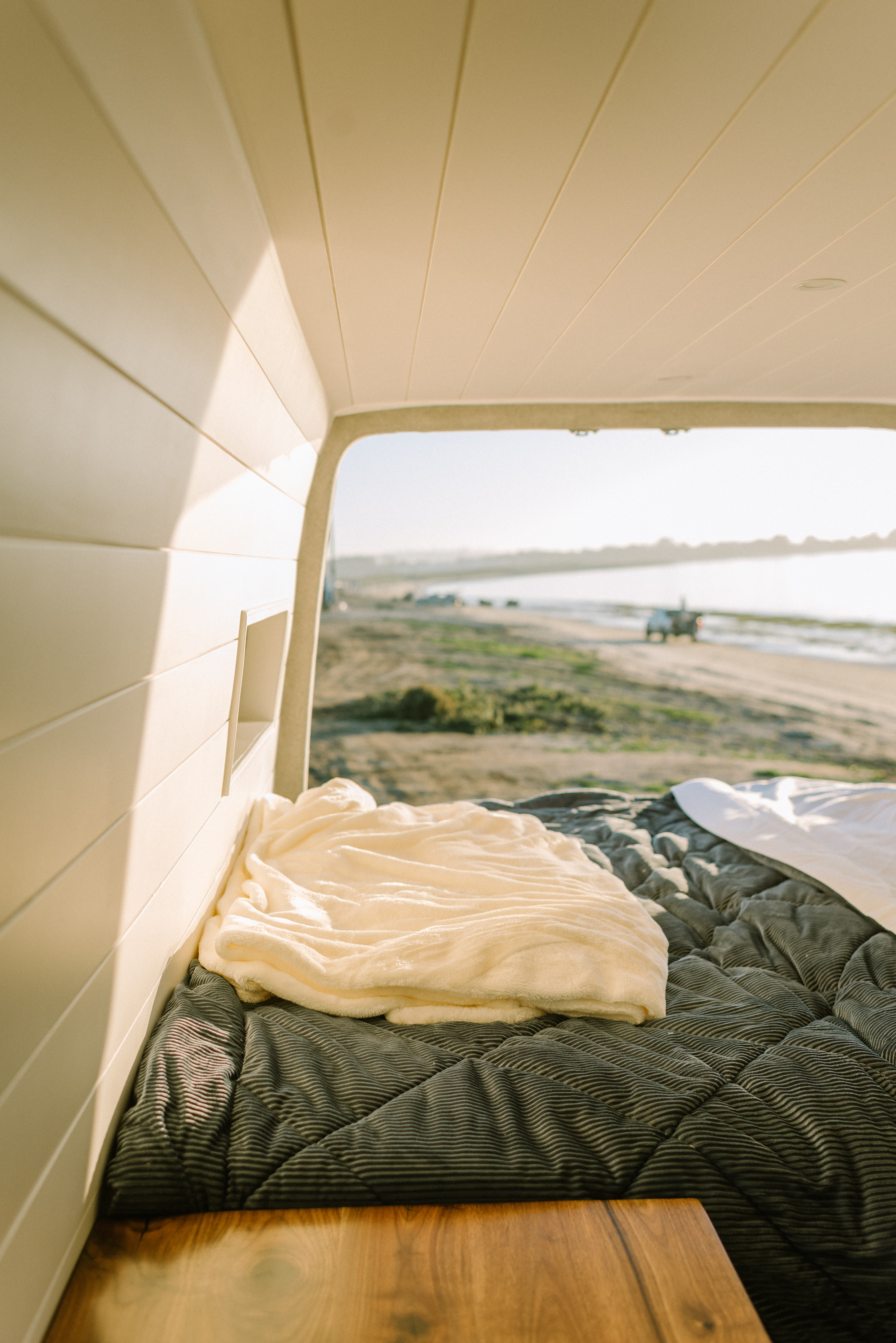 Cozy RV rental interior: a soft bed overlooks a serene beach scene, perfect for relaxing travel.. Mercedes-Benz Sprinter 2021