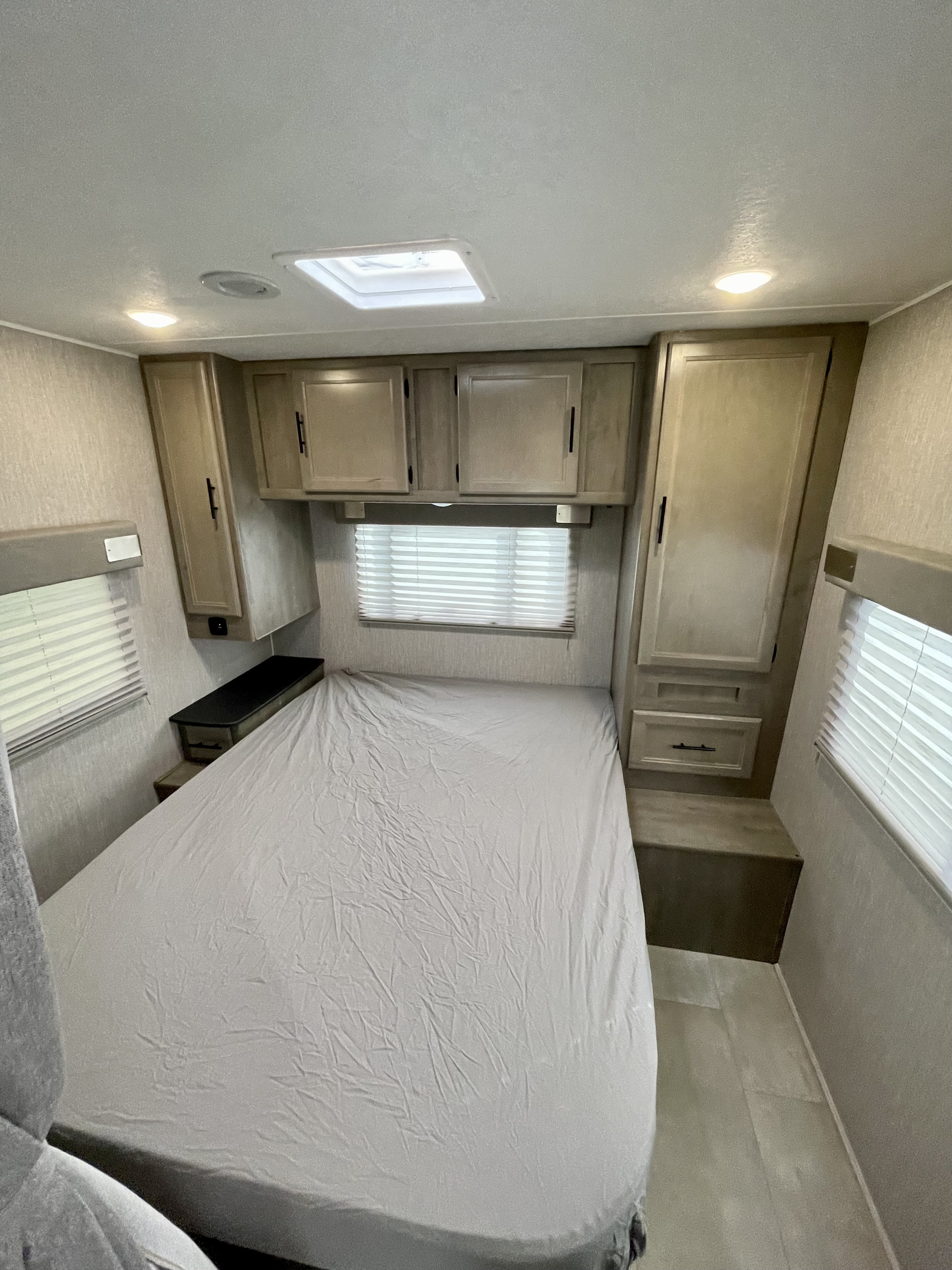 Experience comfort in this RV rental bedroom: light grey bed, overhead cabinets, windows with blinds, and skylight view.. Coachmen Freelander 2021