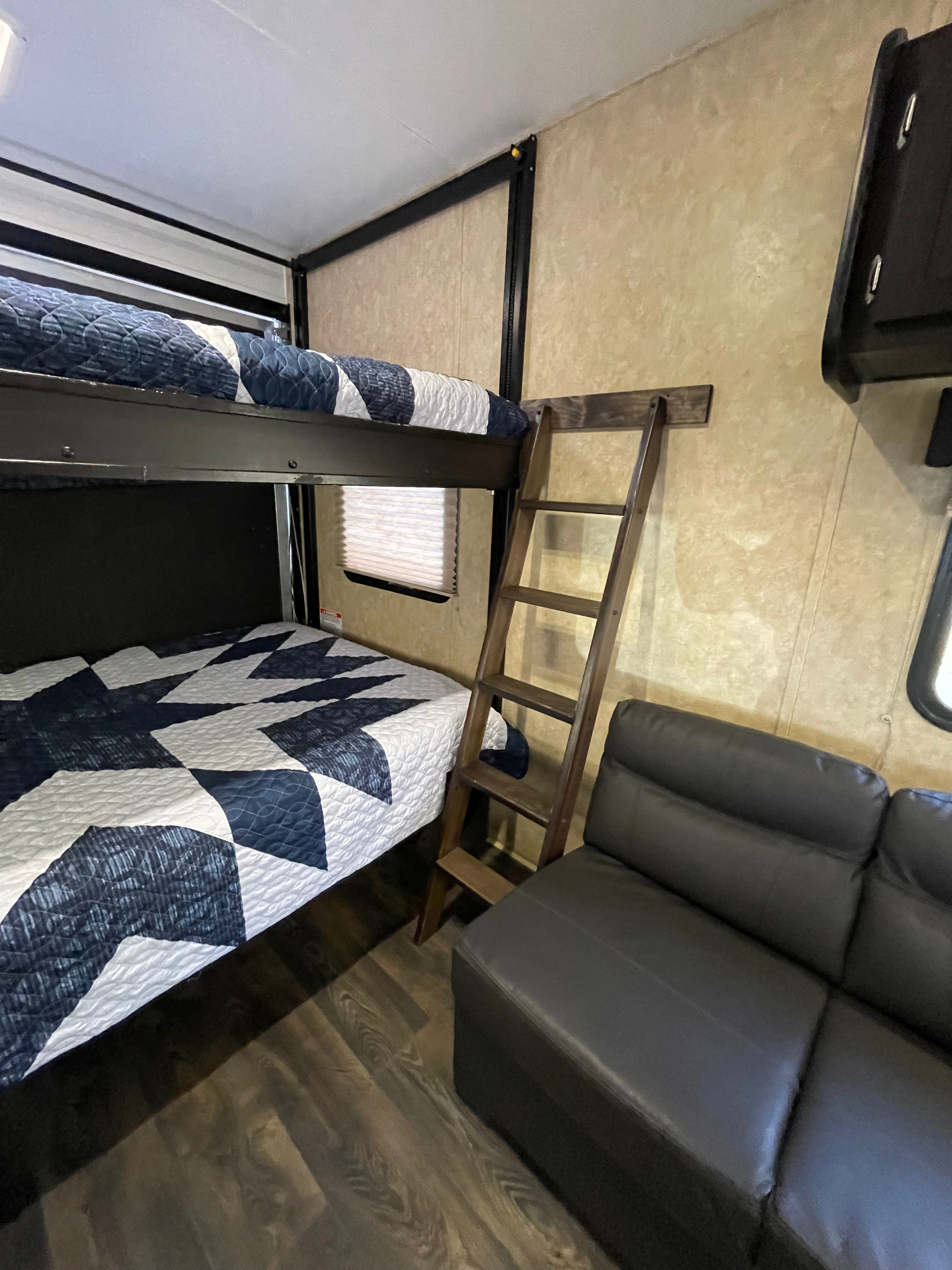 This RV rental interior features cozy bunk beds with bedding, a ladder, and a black sofa, maximizing sleeping and seating space.. Dune Sport Toy Hauler 2017
