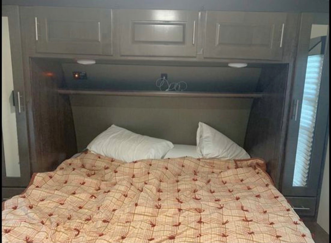 Cozy RV rental bedroom with a made bed, patterned blanket, two pillows, overhead cabinets, and side wardrobe. Ideal for comfortable rest.. Cruiser Rv Corp Stryker 2018