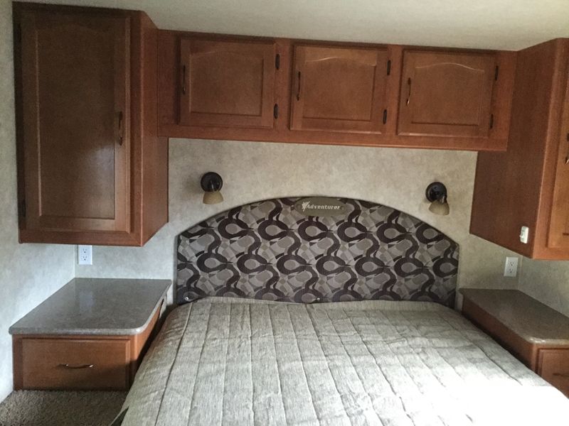 RV rental bedroom: a comfortable bed with a patterned headboard, overhead cabinets, and convenient side storage.. Adventurer 31DS 2014