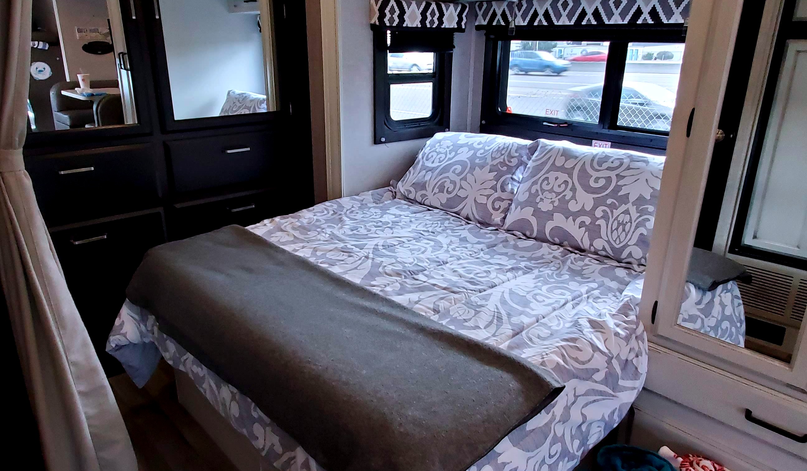 Cozy **RV rental** **bedroom** with patterned **bed**, dark **cabinets**, and **windows** showing outside. Mirrors reflect the interior.. Jayco Redhawk 2022