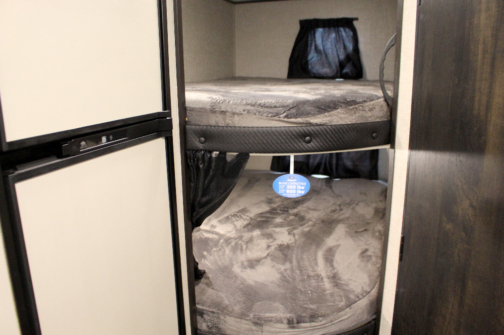 Inside an RV rental: two cozy bunk beds with privacy curtains, next to a fridge. Safety capacity info is visible.. Jayco Jay Flight SLX 224BH 2022