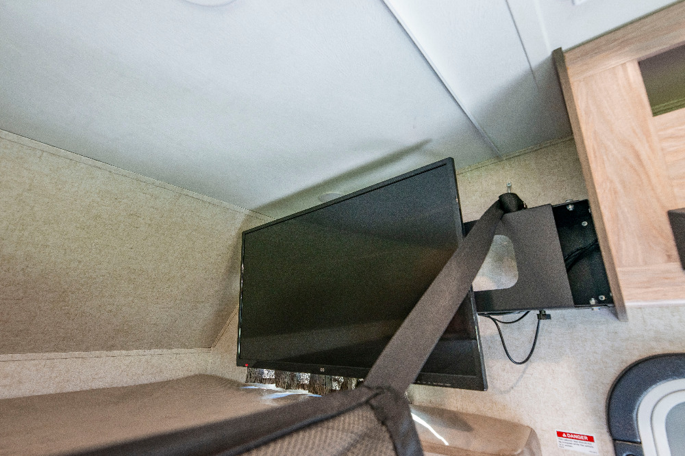 RV rental interior: A black flat-screen TV, securely fastened by a dark strap to its wall mount, within a recreational vehicle.. Forester LE 2018