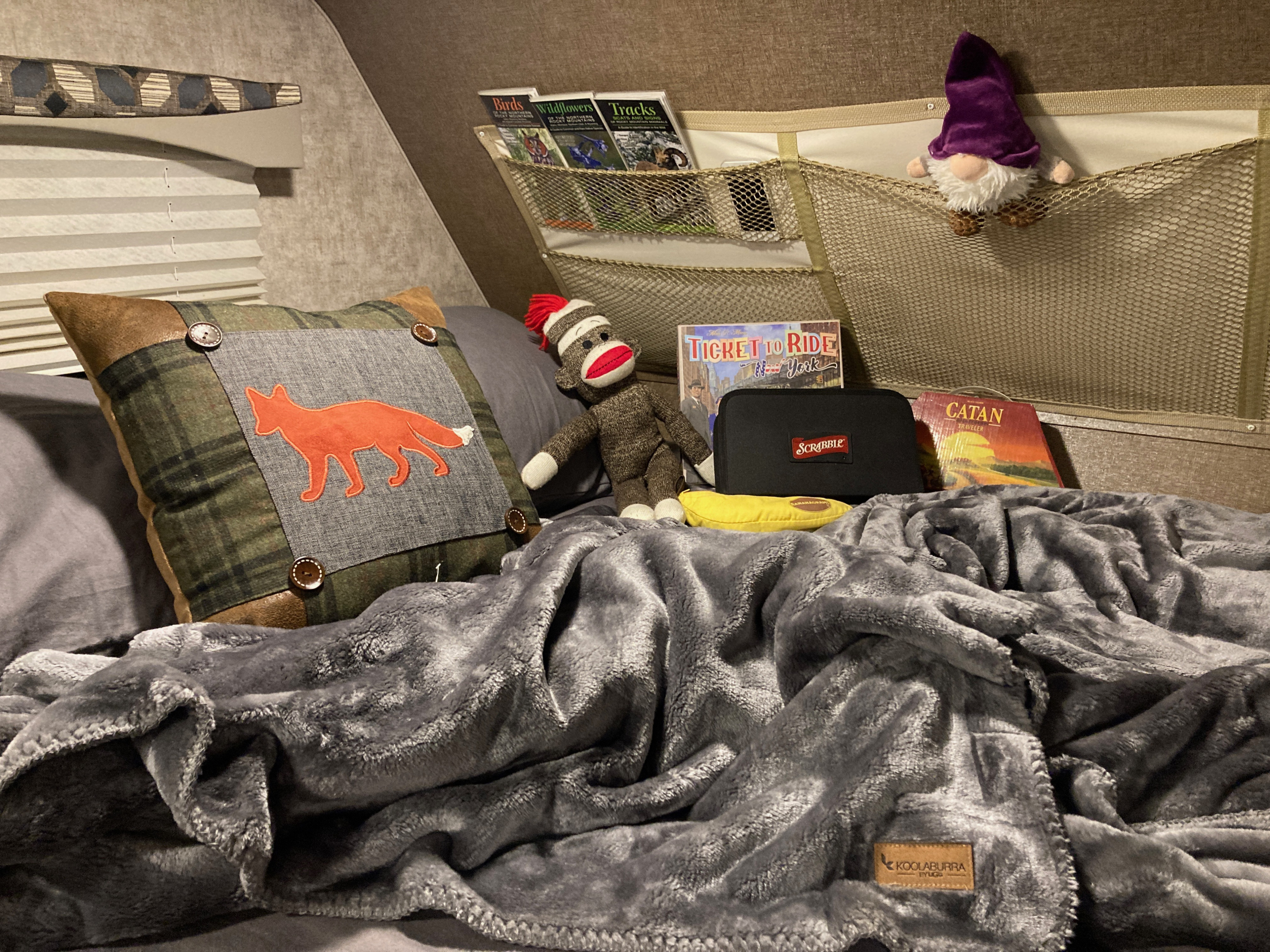 Cozy RV rental bed: plush blanket, games (Catan, Ticket to Ride, Scrabble), nature guides, and fox pillow.. Adventurer Class C 23RB 2019