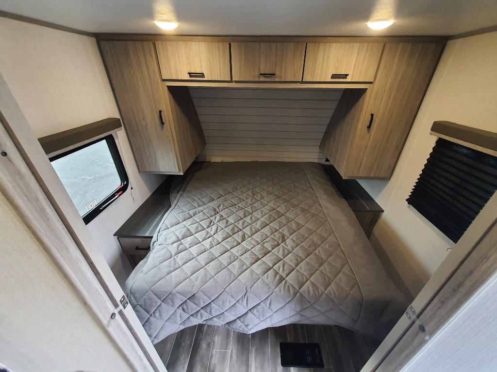 Inside an RV rental: a cozy bedroom with a quilted bed, overhead cabinets, and bedside tables. Perfect for your next adventure.. Keystone RV Passport SL 2022
