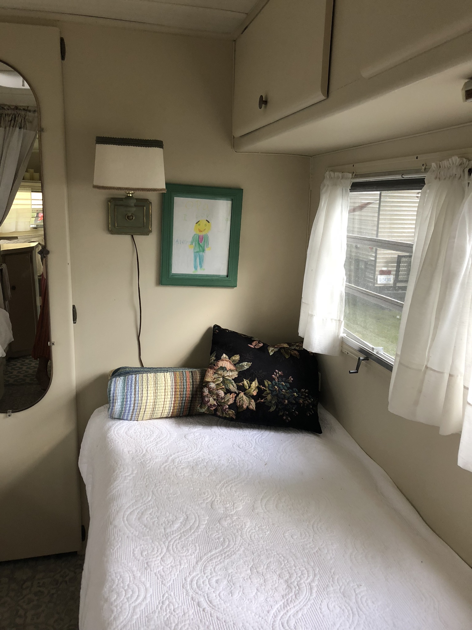 Cozy RV rental interior: single bed with pillows, wall lamp, child's drawing, & window. Ideal for compact comfort.. Holiday Rambler Vacationer 1969
