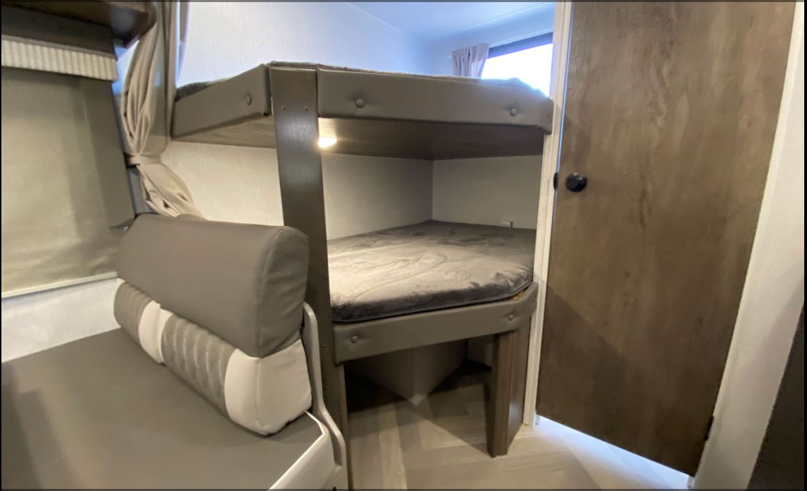 Cozy bunk beds in this RV rental's interior, featuring a lower mattress, an adjacent dinette seat, and a privacy door.. Forest River Salem Cruise Lite 2022