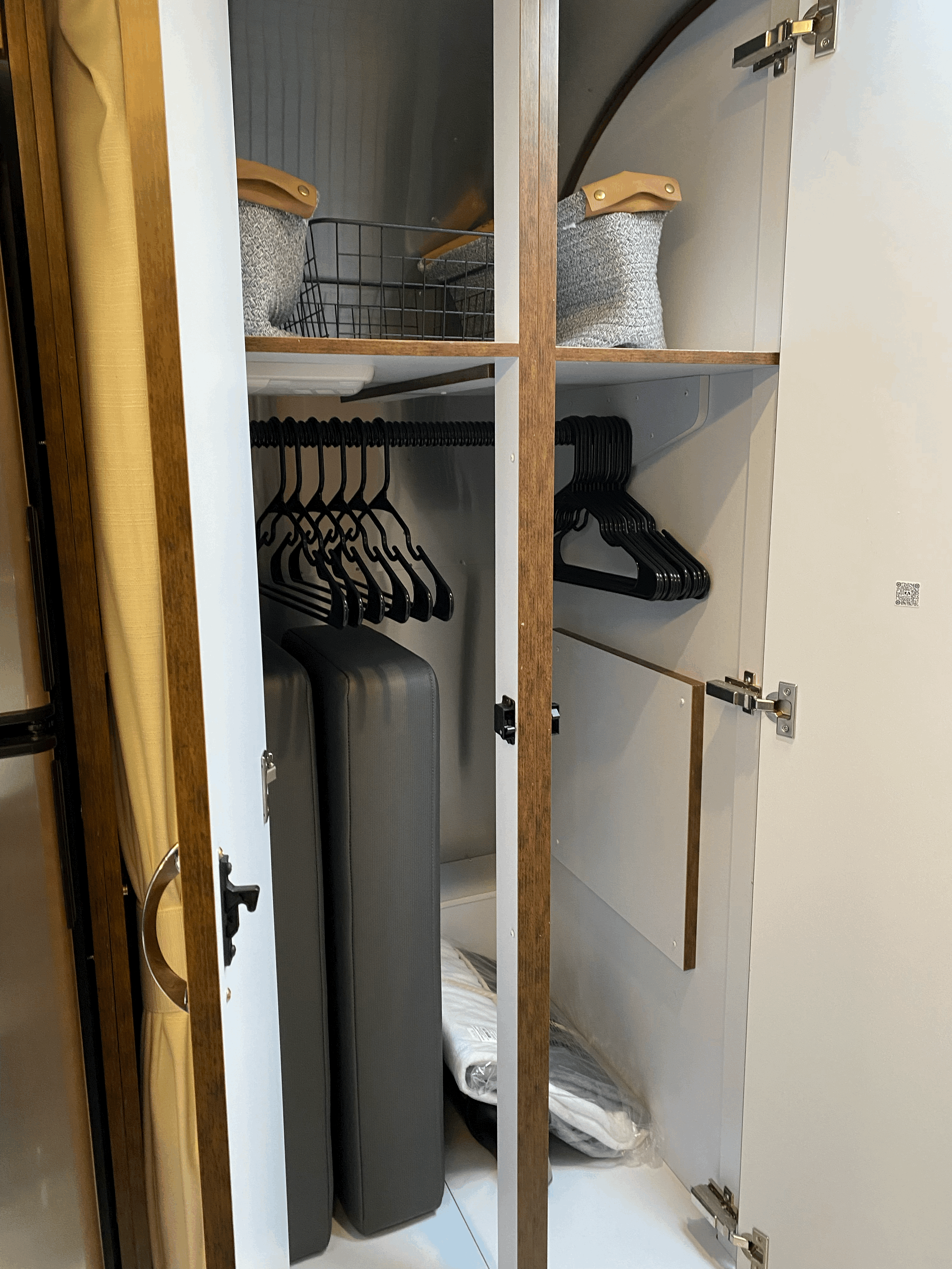 Inside an RV rental: a compact, organized wardrobe with upper storage bins, hanging clothes hangers, and lower essentials storage.. Airstream Globetrotter 2022