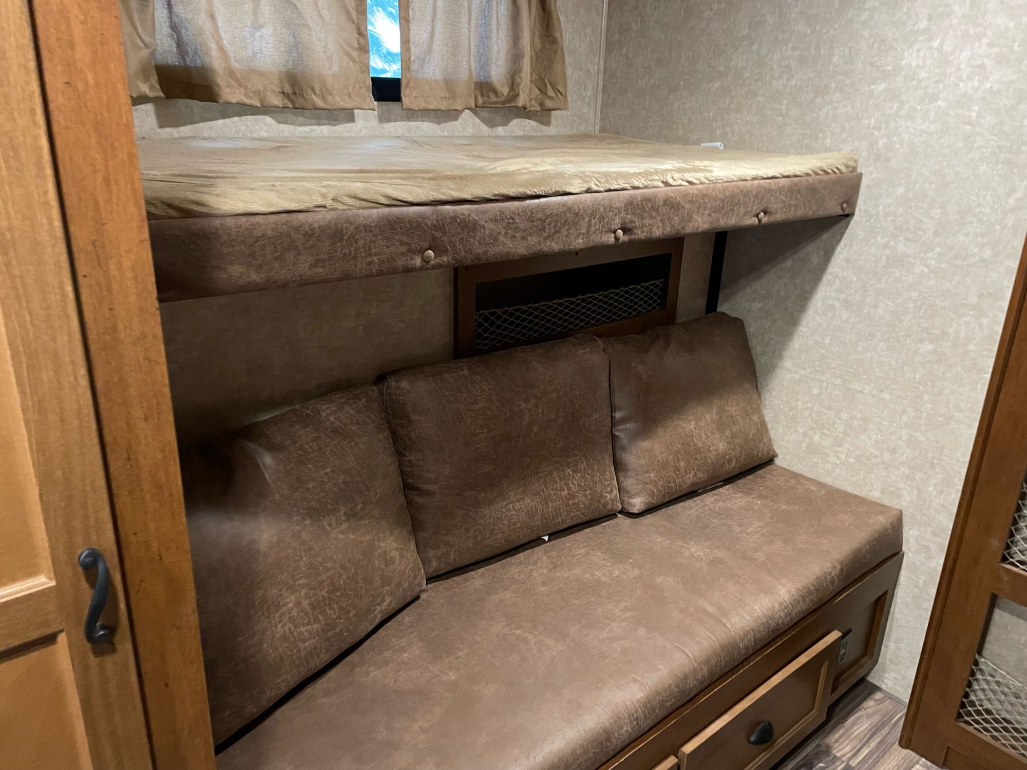 RV rental bunk bed with light cover above a brown sofa. Interior shows compact living space & storage.. Open Range Light 2017