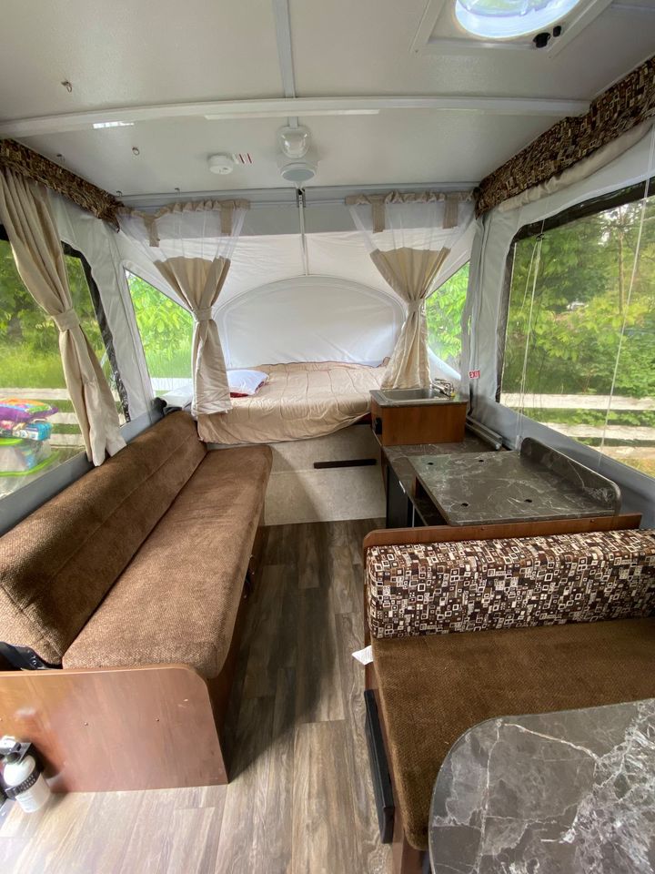 RV rental interior: large bed, sofa, dinette. Brightly lit by big windows with drapes. Wood-look floor. Ready for your adventure!. Jayco Sport 2016