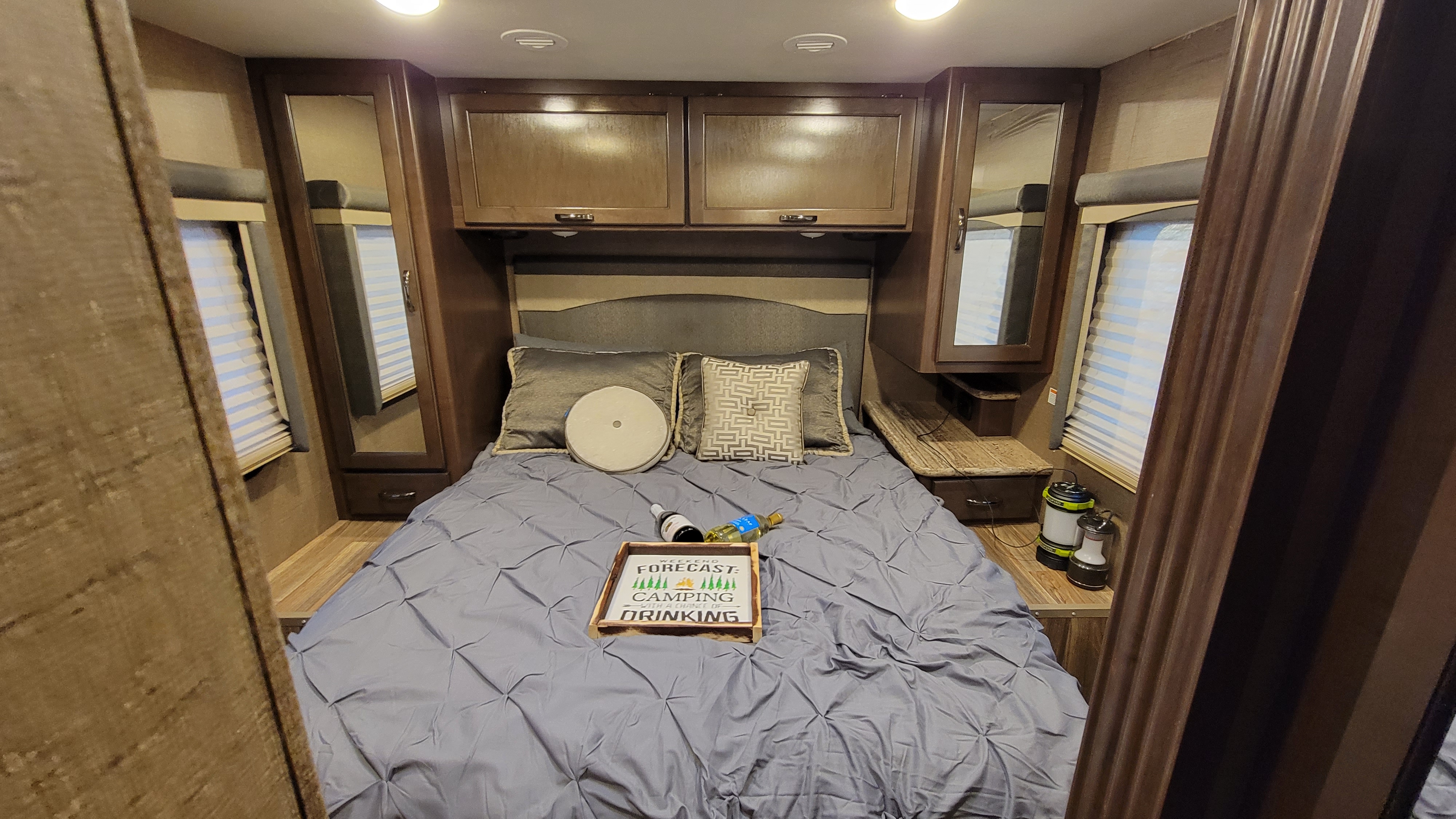 Cozy RV rental bedroom with dark wood cabinets, a queen bed, and camping-themed decor. Perfect for your next adventure.. Thor A.C.E. 2018