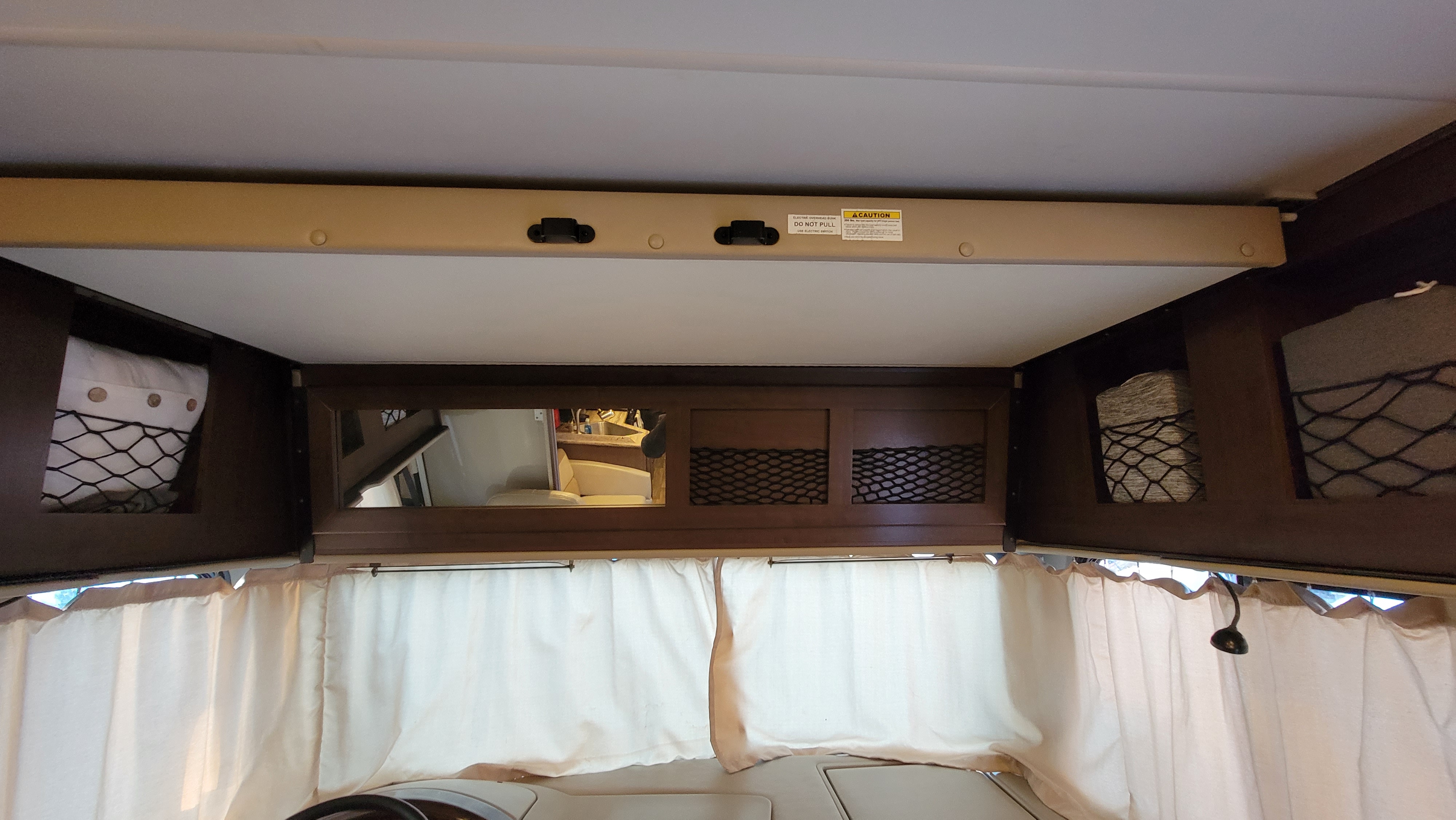 RV rental interior showing an overhead bed/bunk, storage nets, and curtains, highlighting a compact living area.. Thor A.C.E. 2018