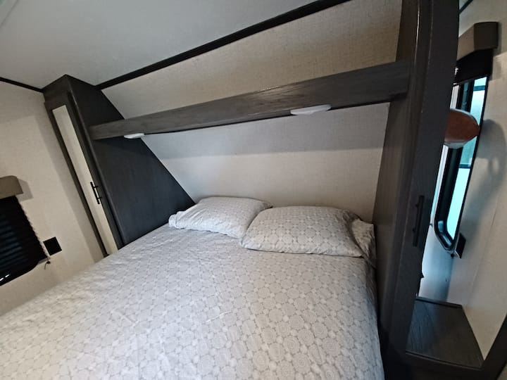 RV rental bedroom featuring a comfortable bed, overhead shelf with lights, and built-in side storage, ideal for your journey.. Dutchmen Aspen Trail 2021
