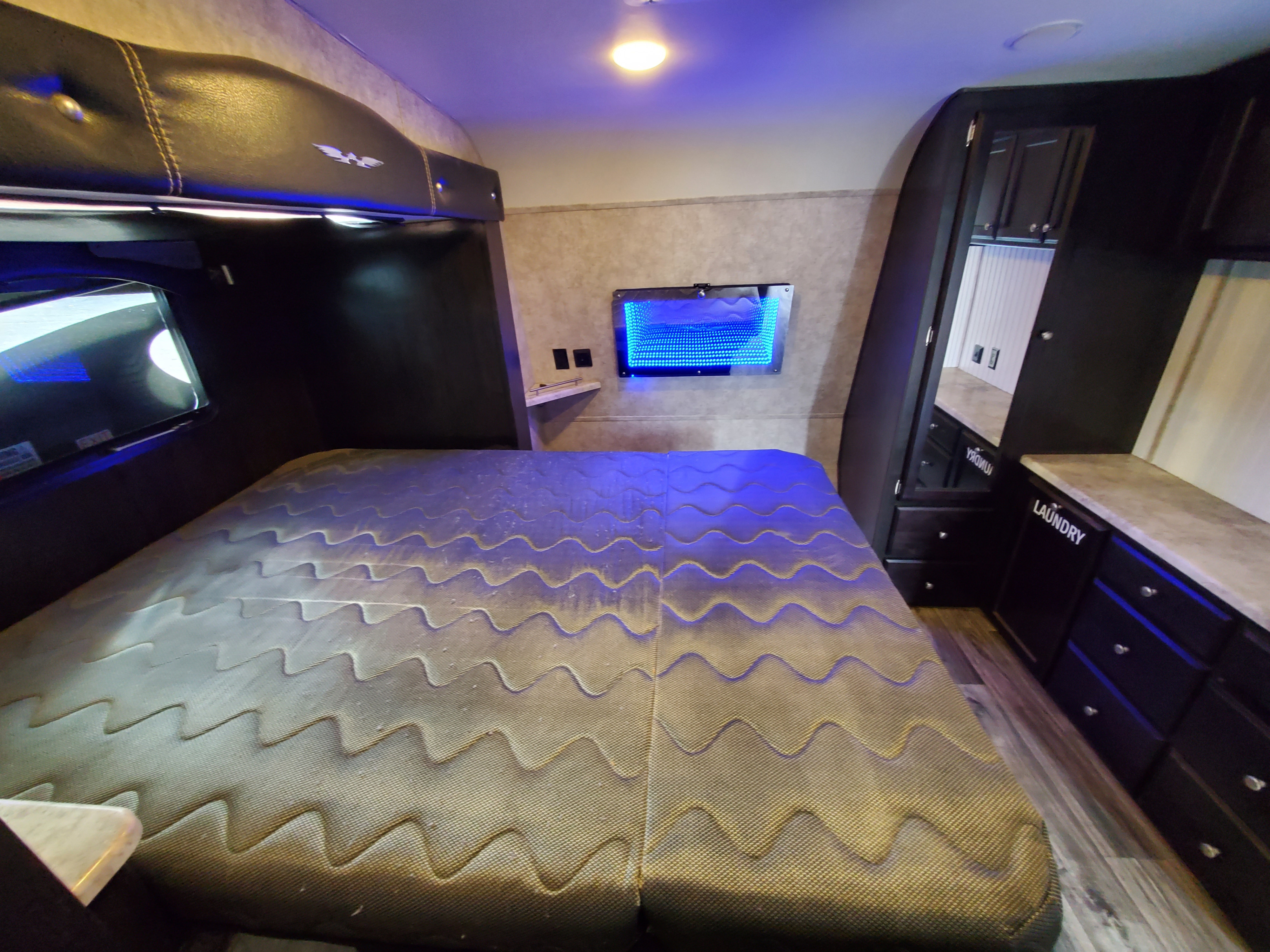 Cozy RV rental bedroom featuring a wavy bed, blue LED lighting, and dark wood cabinets with ample storage.. Weekend Warrior jj2400 2019