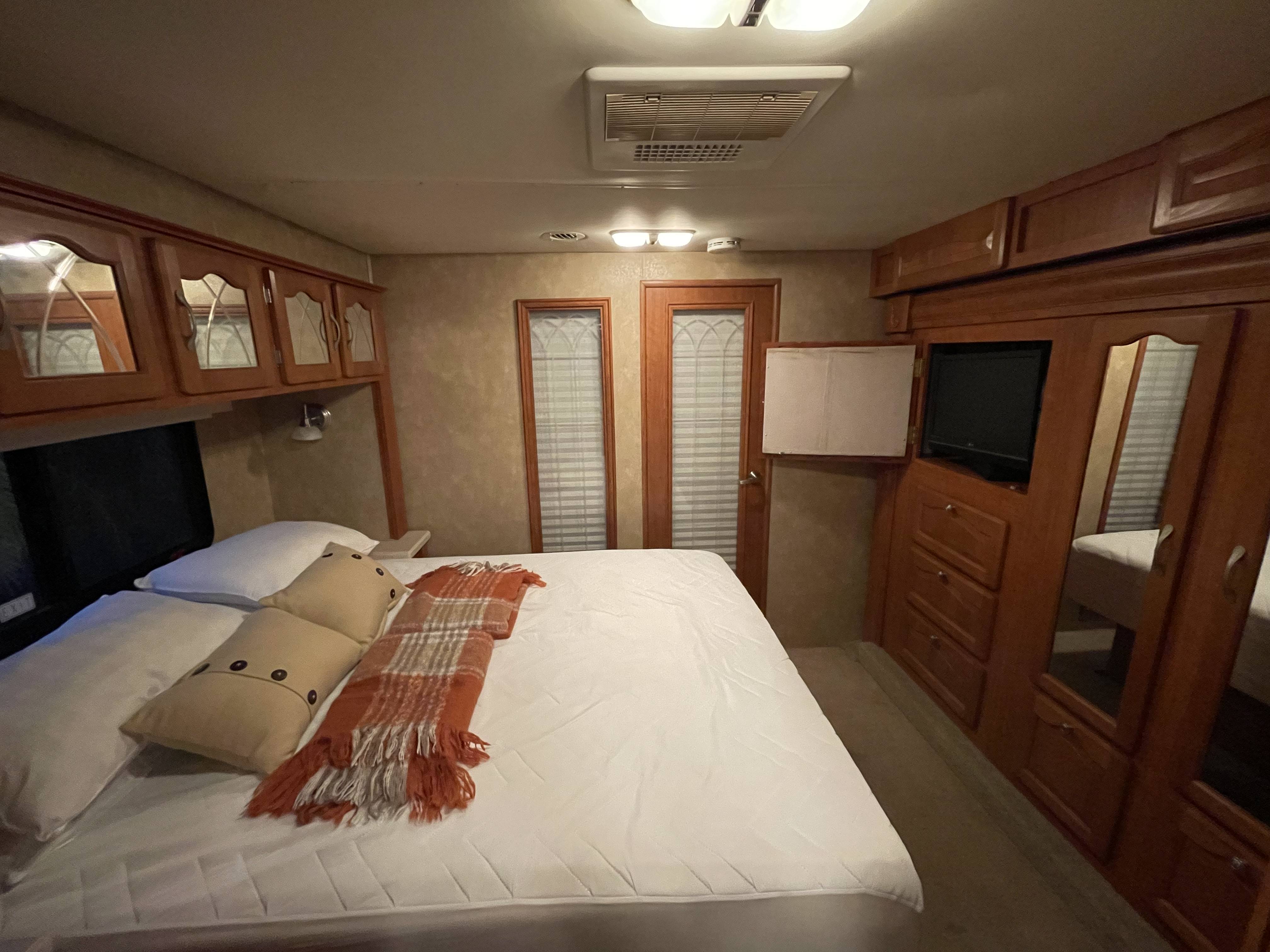 Step into comfort! This RV rental bedroom showcases a cozy bed, ample storage, and a TV, ideal for road trip relaxation.. Georgetown XL 2008