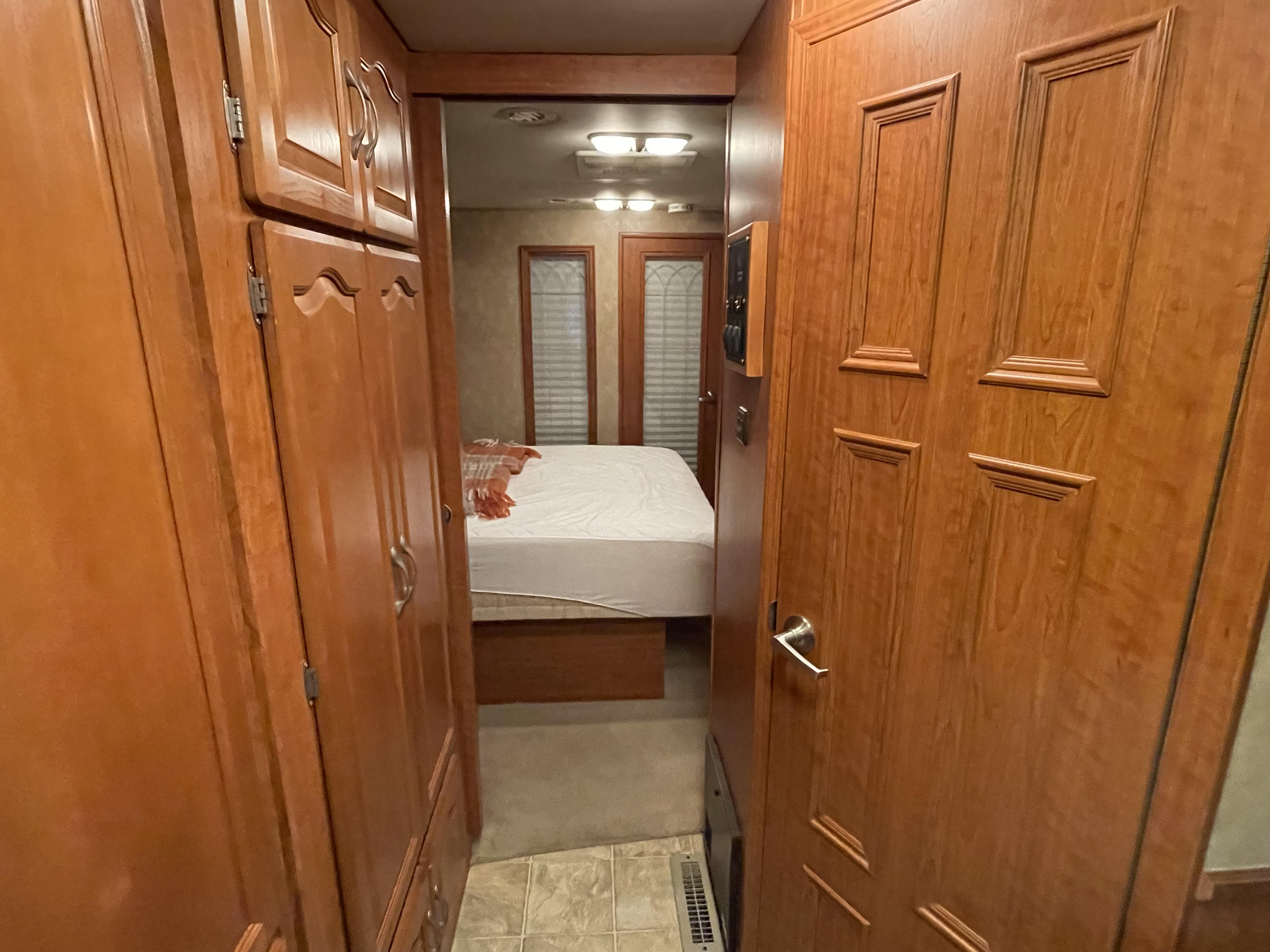 This rv rental features a compact bedroom with a bed & blinds, seen from a hallway lined with warm wooden cabinets & a door.. Georgetown XL 2008