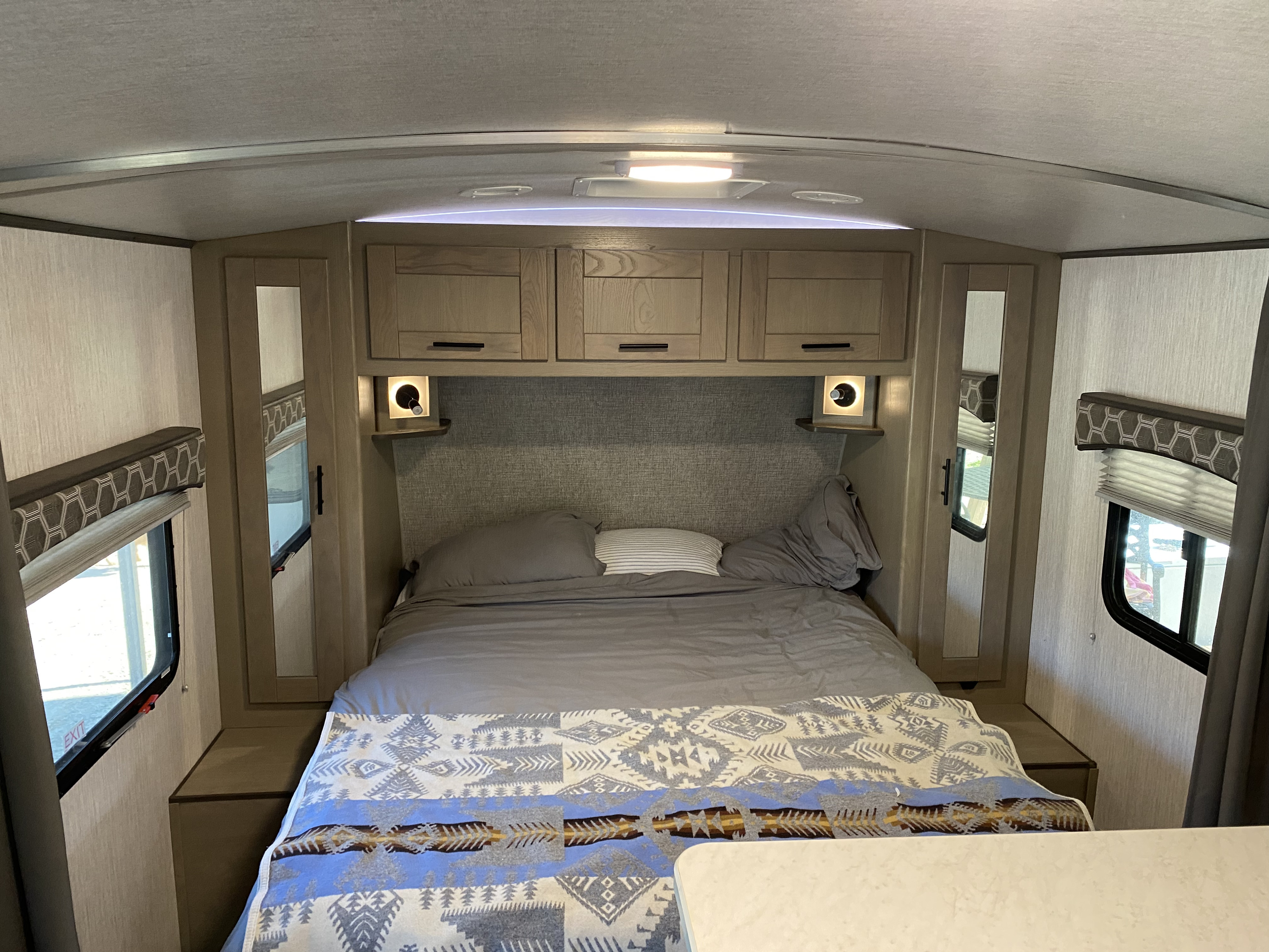 Cozy RV rental bedroom with comfortable bed, overhead cabinets, and lighting, perfect for travel.. Shadow Trailers Cruiser 2020