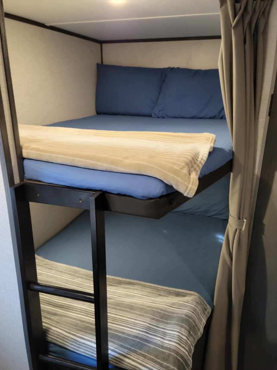 Cozy RV rental bunk beds with blue sheets, a tan blanket on top, and a grey striped blanket on the bottom.. Aspen Trail Aspen Trail Trailer 2021