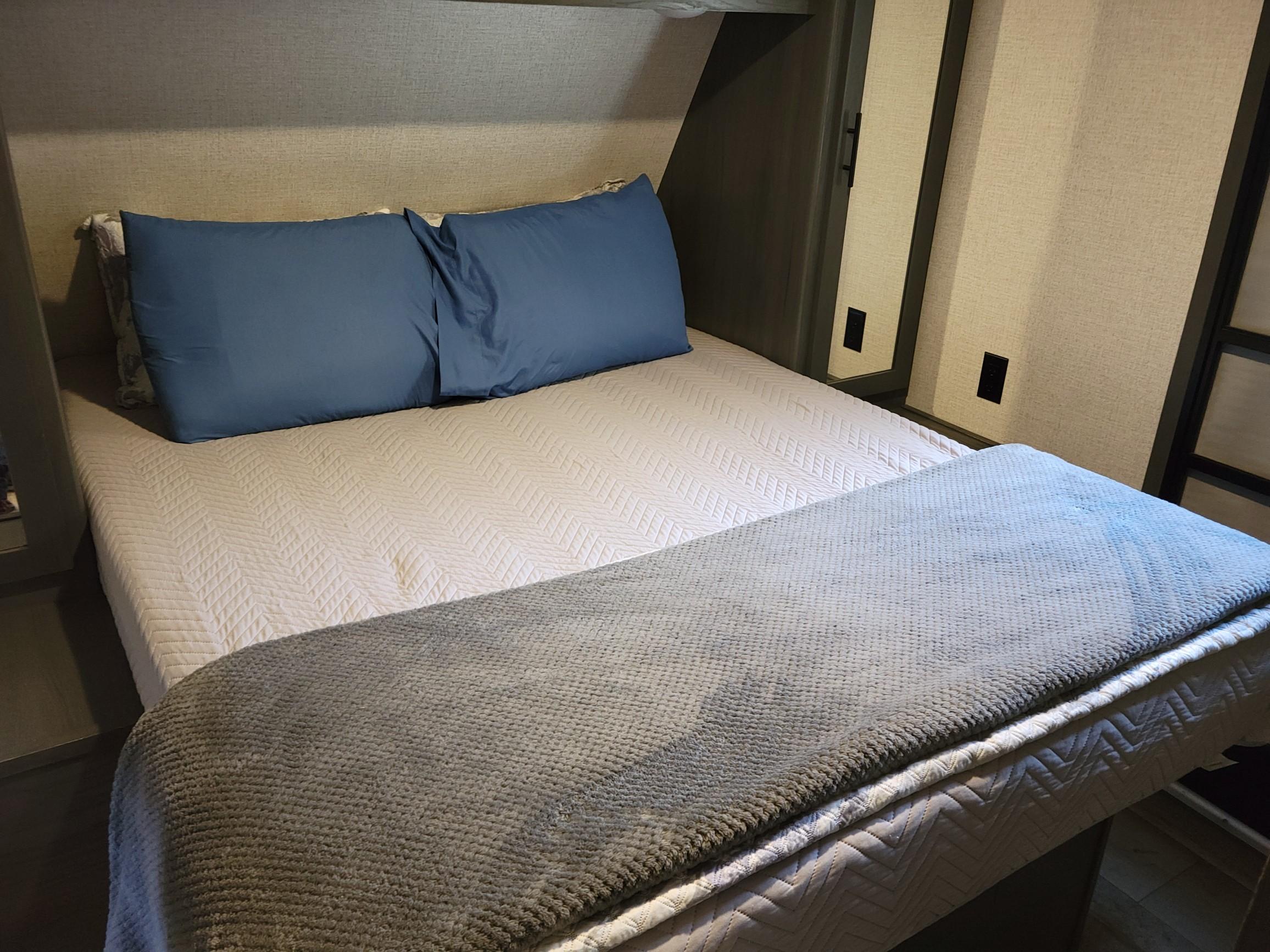 Inside a comfortable RV rental bedroom, featuring a neatly made bed with blue pillows, a white quilted blanket, and a soft gray throw.. Aspen Trail Aspen Trail Trailer 2021