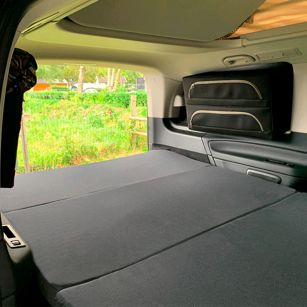 RV rental: Camper van interior with a large, dark gray fold-out bed and side storage, overlooking a green outdoor scene.. Mercedes Marco Polo 2022