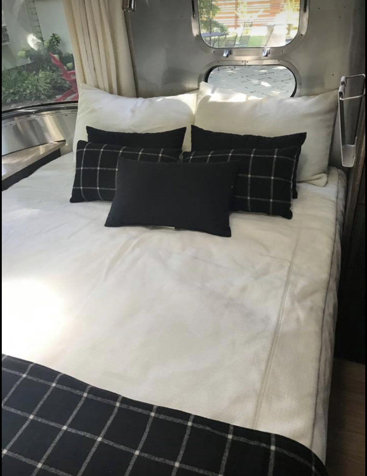 Cozy Airstream RV rental interior features a comfortable bed with white bedding, black and plaid pillows, and windows.. Airstream International 2016