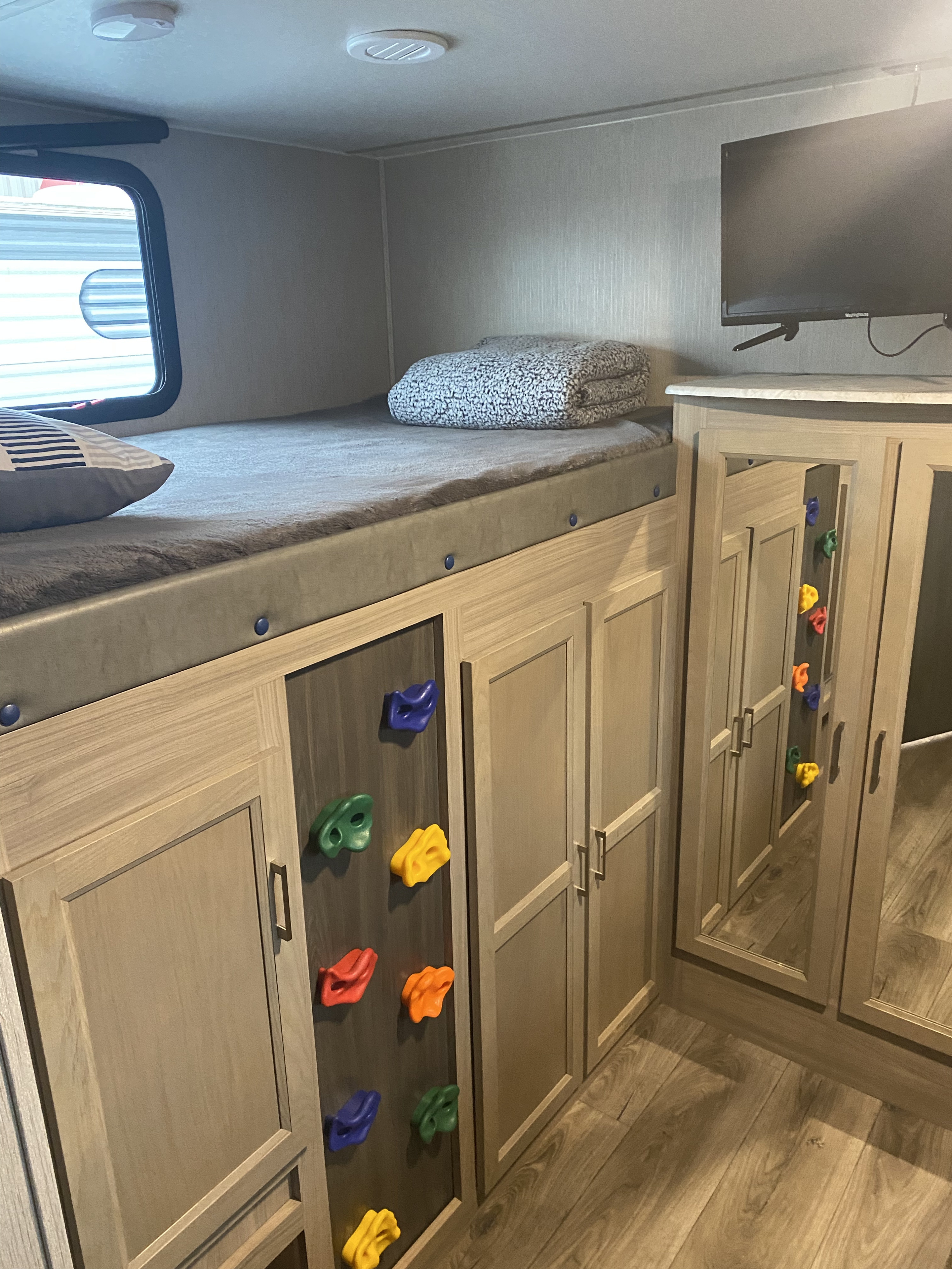Inside an RV rental: a kid-friendly bunk bed area with a small climbing wall, storage, and TV.. Coachmen Liberty 2020