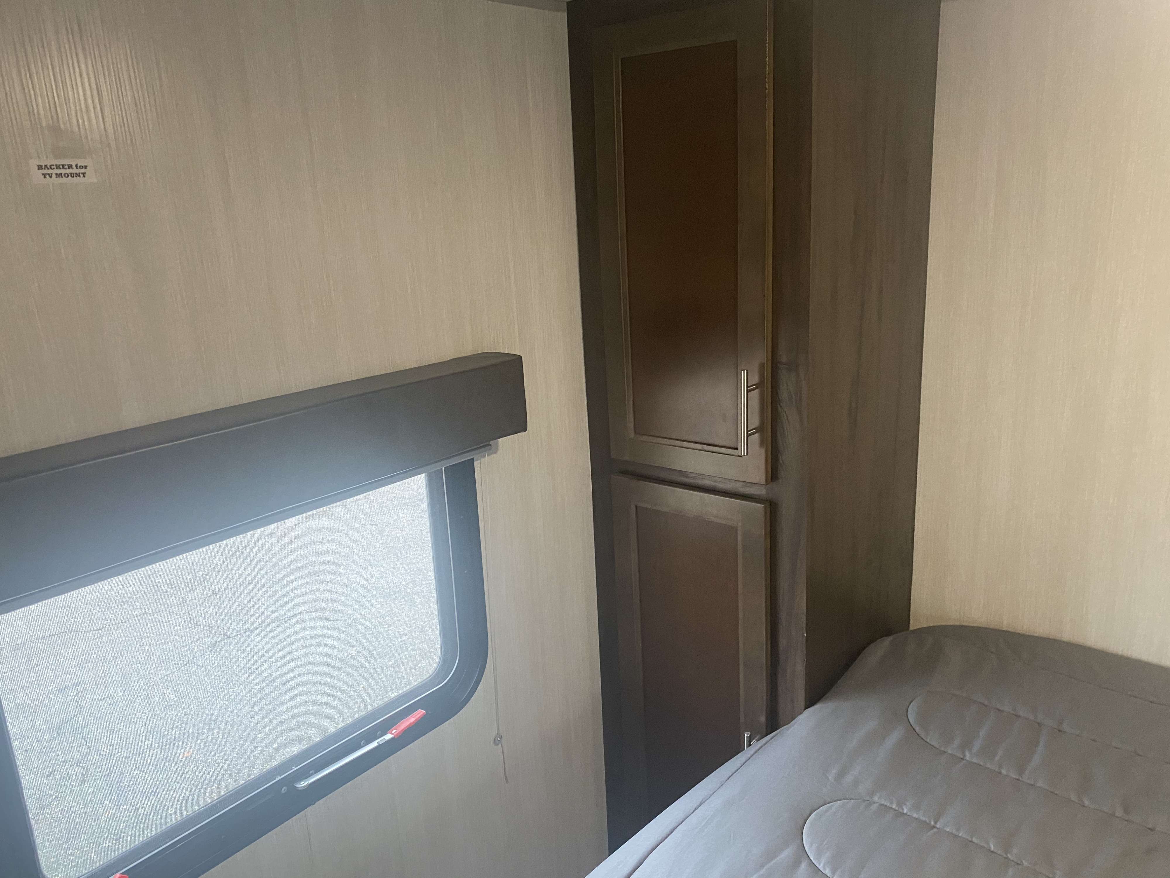 Cozy RV rental interior: A bedroom area featuring a light gray quilted bed, large window, and dark wood storage cabinet on the right.. Forest River Cherokee Grey Wolf 2019